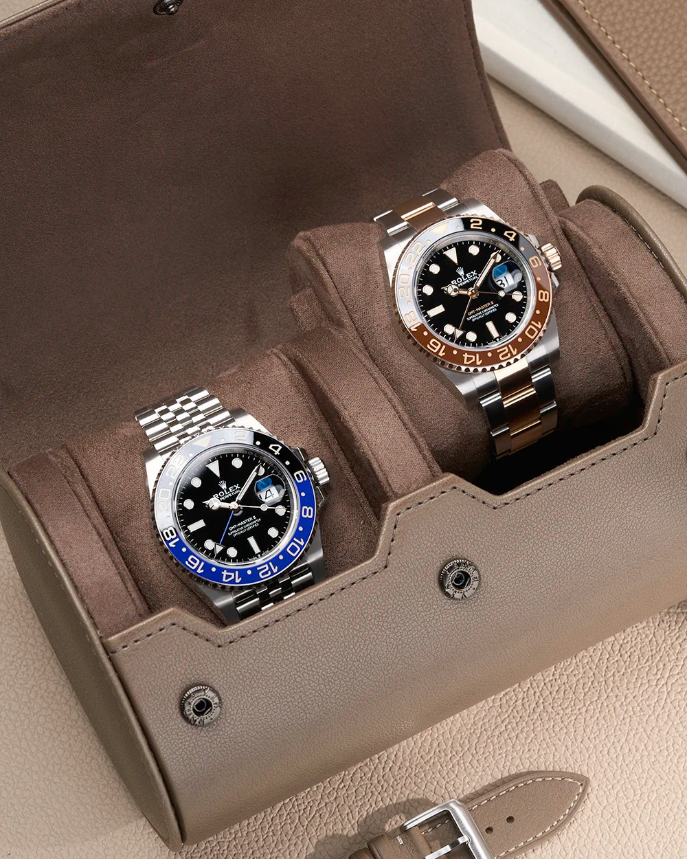 Rolex GMT Batgirl and Rolex GMT Rootbeer in a watch roll on a taupe surface