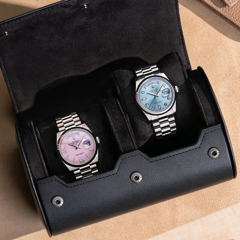 Black 2 slot watch roll with soft suede interior holding two Rolex watches displayed on beige surface