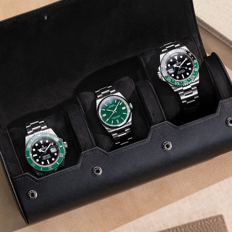 Black 3 slot watch roll with suede interior holding three green Rolex watches on beige surface