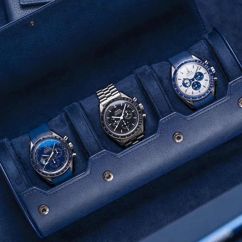 Navy blue 3 slot watch roll with suede interior holding three Omega watches on blue surface