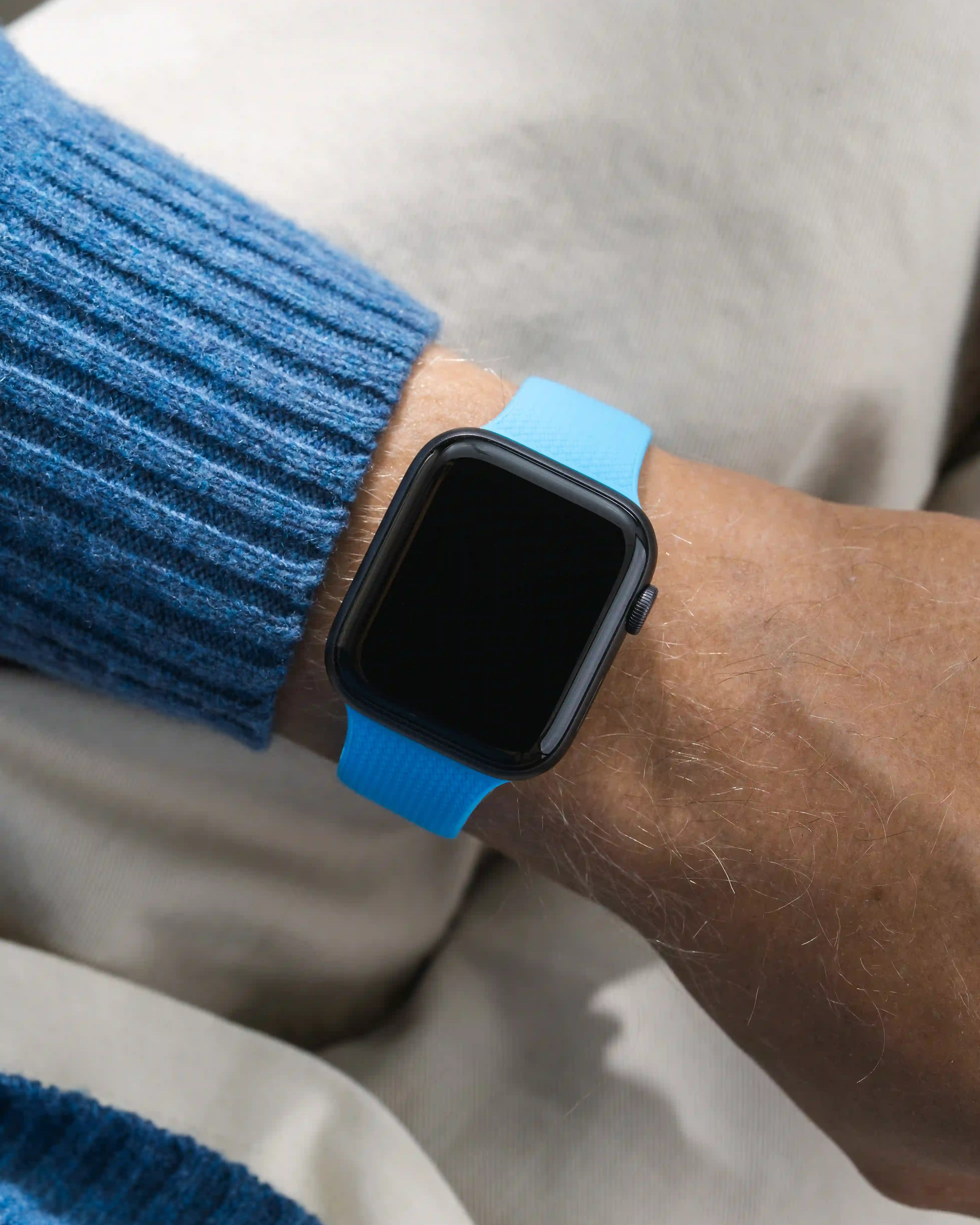 Smartwatch with a blue band on a wrist, wearing a blue sweater.