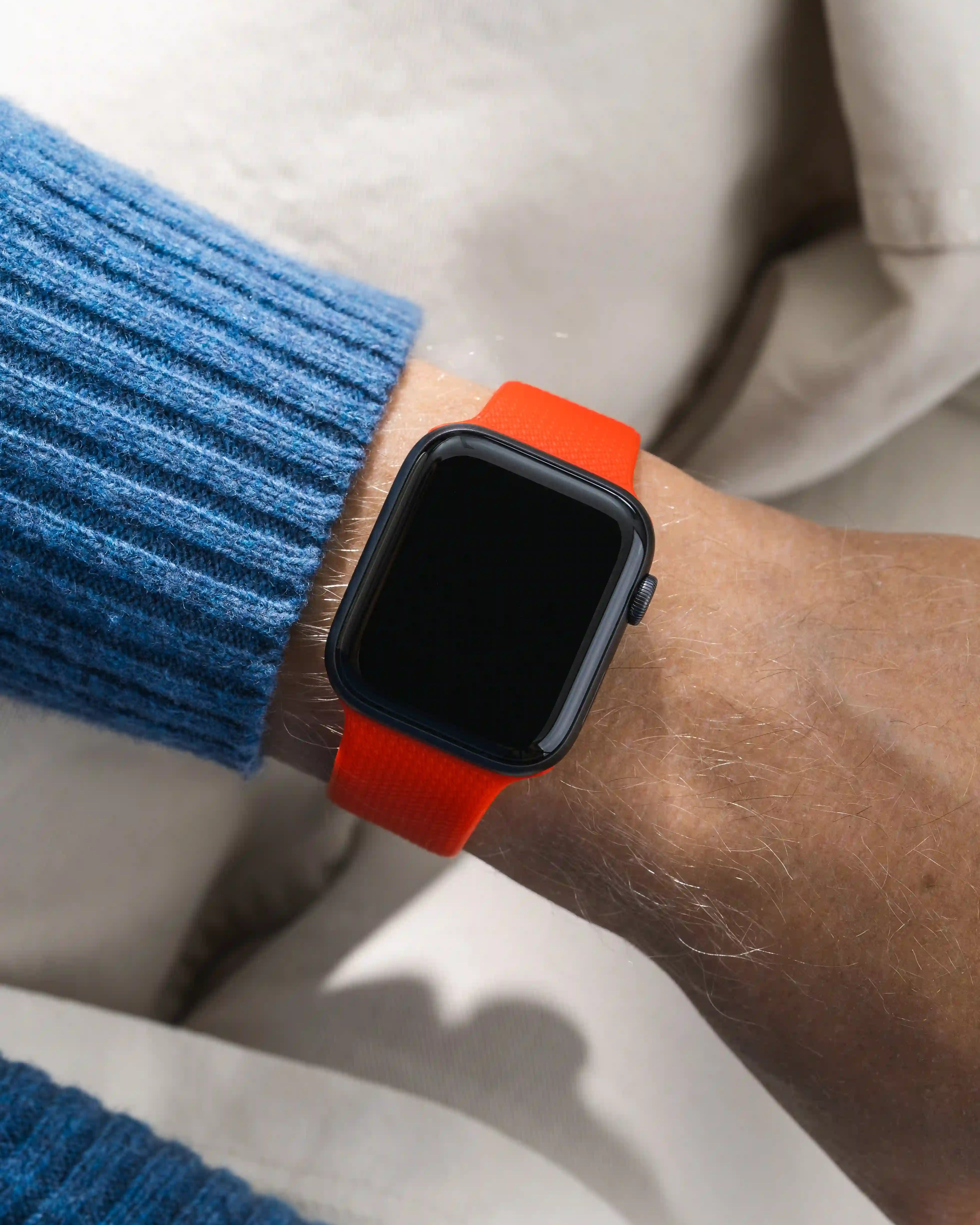 Smartwatch with an orange red on a wrist wearing a blue sweater.