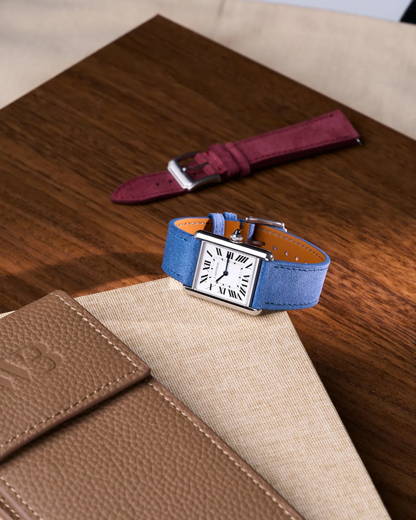 Baltic Blue suede strap on Cartier Tank watch placed on beige leather | styled scene with burgundy strap in background