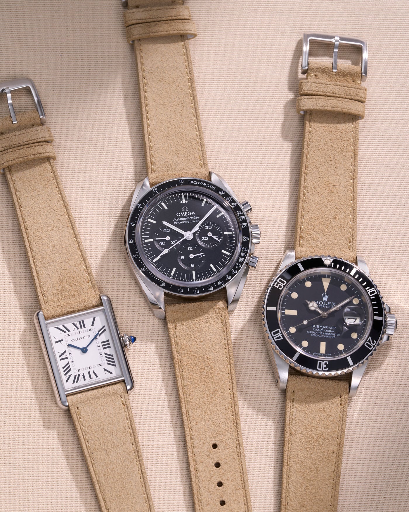 Cartier Tank, Omega Speedmaster and Rolex Submariner watches with beige suede straps.
