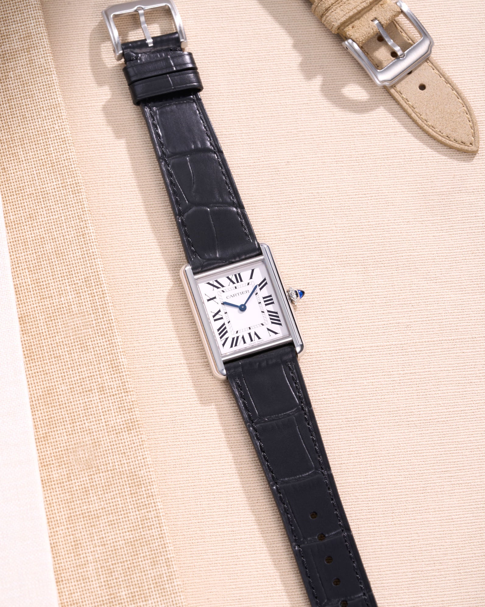 Flat lay of Cartier Tank Must Large watch on black embossed alligator leather strap, displayed on beige fabric background