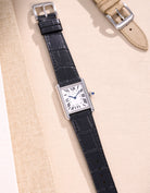 Flat lay of Cartier Tank Must Large watch on black embossed alligator leather strap, displayed on beige fabric background