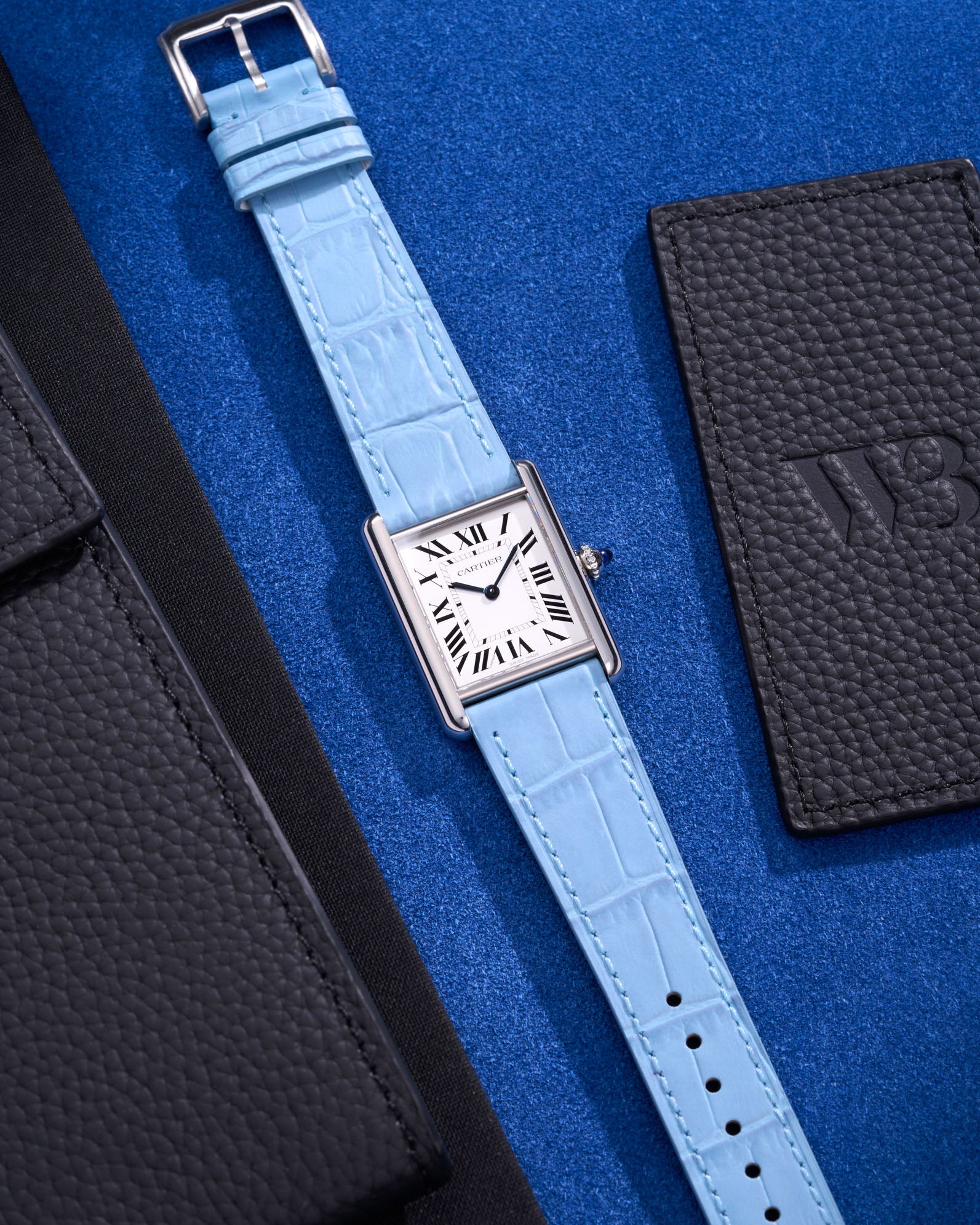 Flat lay of Cartier Tank Must Large watch on sky blue embossed alligator leather strap, displayed on blue fabric background