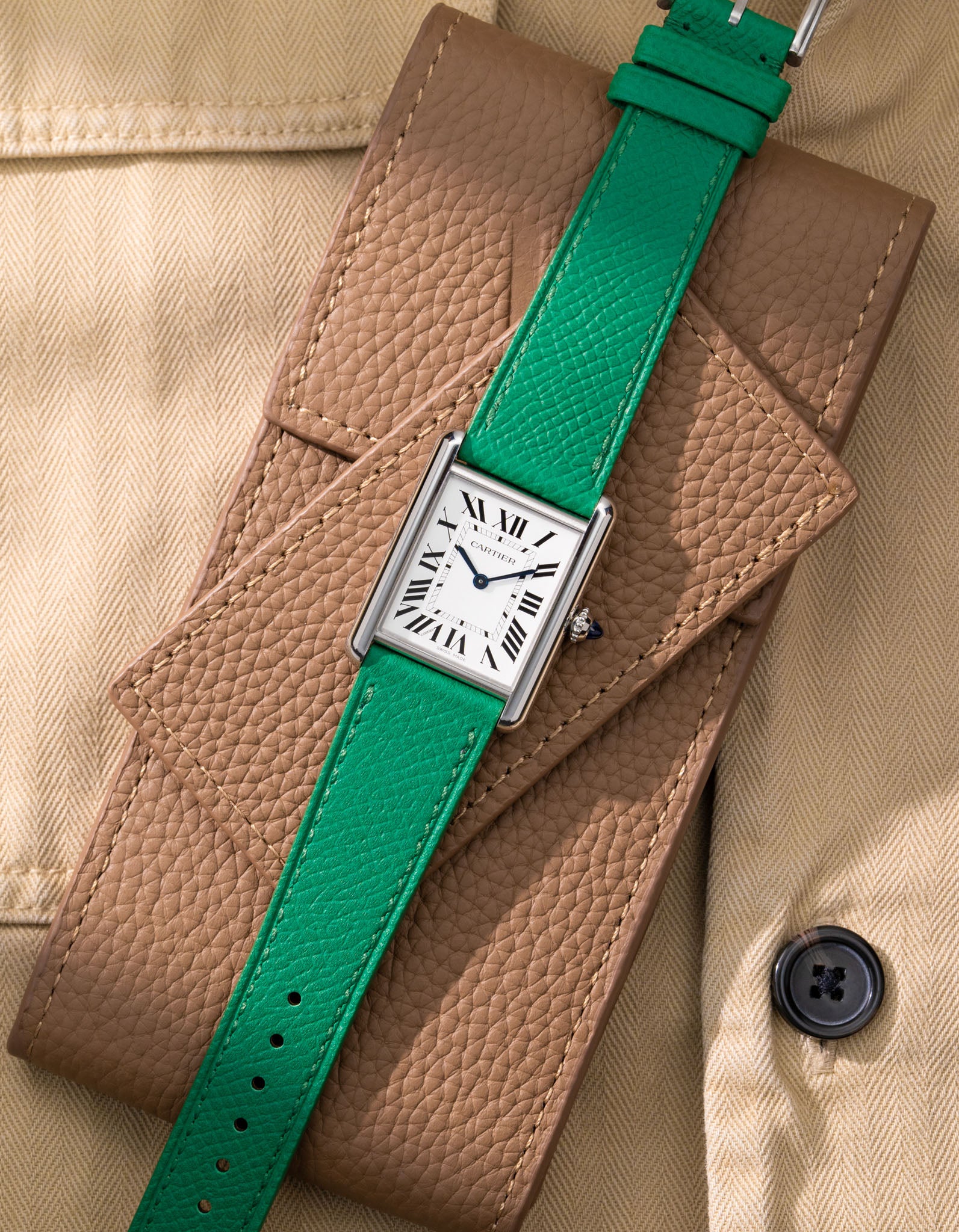 Cartier Tank Must Large with green epsom leather strap, flat lay on brown watch pouch with beige fabric background