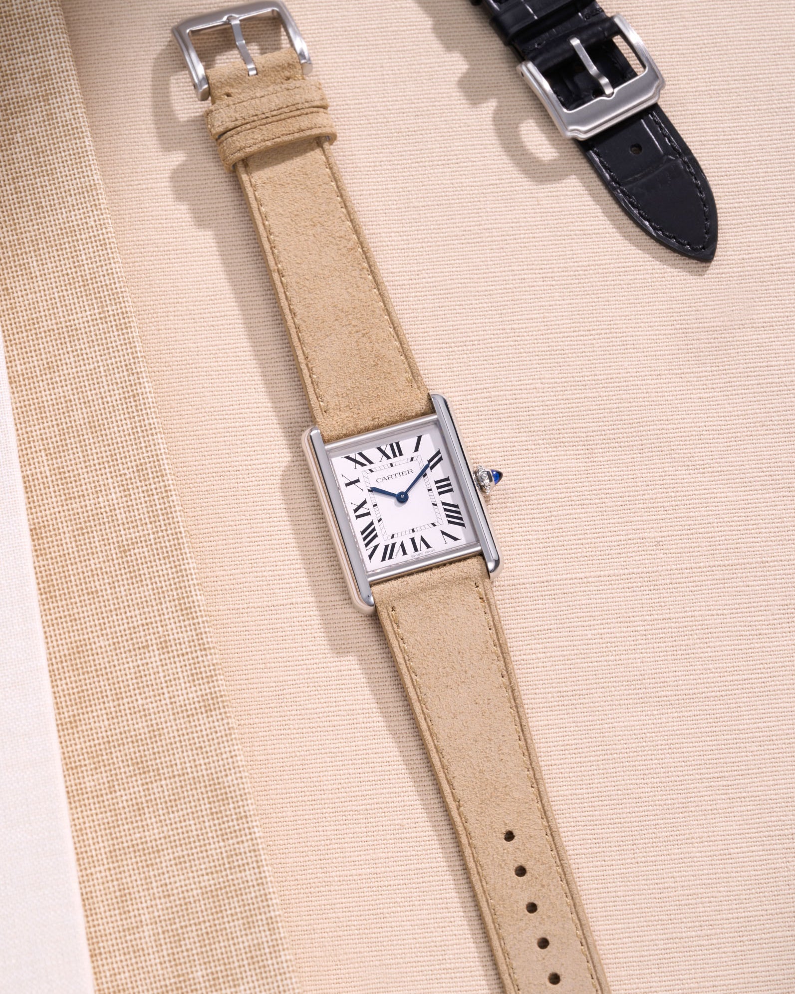 Cartier Tank Must Large watch with Beige Suede leather strap, lying flat on beige leather-textured background