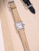 Cartier Tank Must Large watch with Beige Suede leather strap, lying flat on beige leather-textured background
