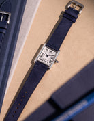 Cartier Tank Must Large with Dark Blue Suede leather strap, flat lay on textured beige surface with clasp visible