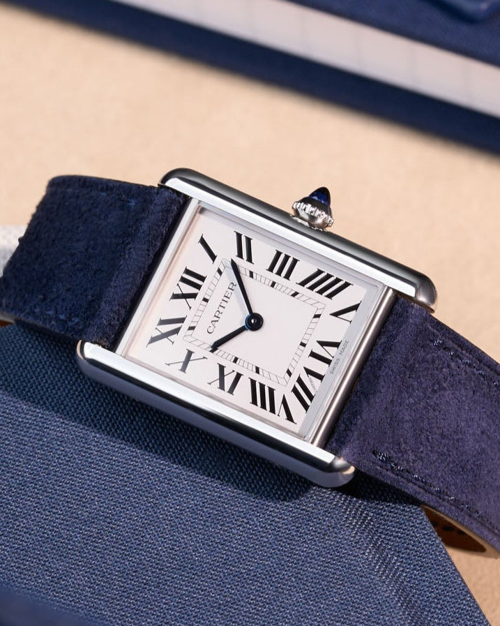 Cartier Tank Must Large with dark blue suede leather strap, shown in a flat lay on fabric surface
