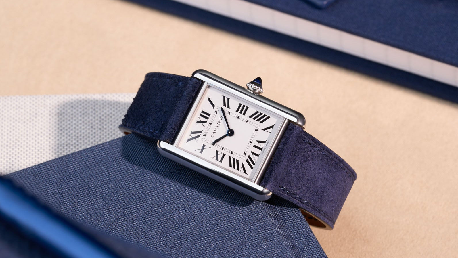 Cartier Tank Must Large with dark blue suede leather strap, shown in a flat lay on fabric surface