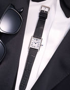 Cartier Tank Must Large with black embossed alligator leather strap, styled flat on white shirt and black suit with sunglasses beside