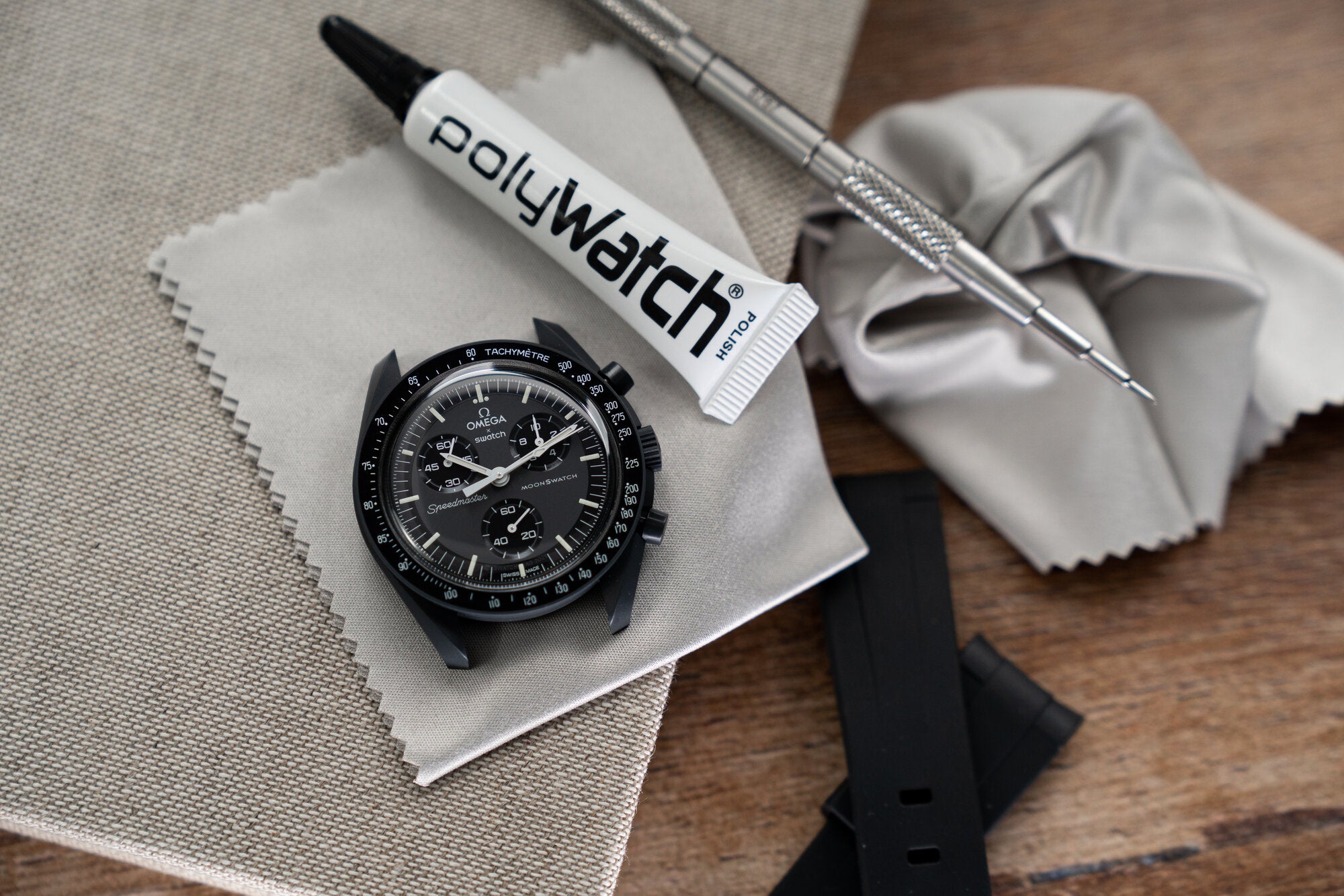 MoonSwatch watch being cleaned with Polywatch polish, spring bar tool and microfiber cloth laying beside