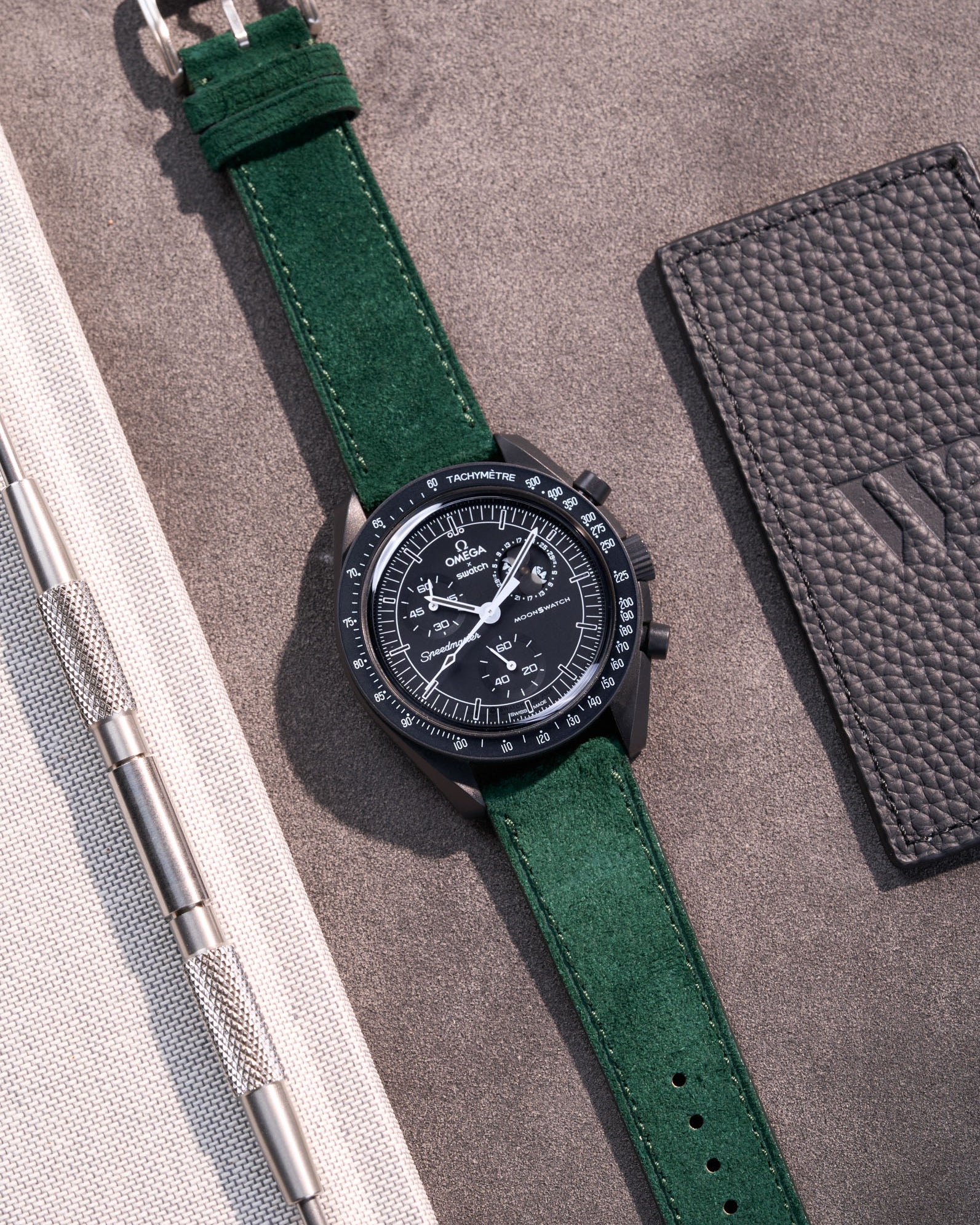 Flat lay Moonswatch Mission to the Moonphase New Moon with Dark Green suede leather strap