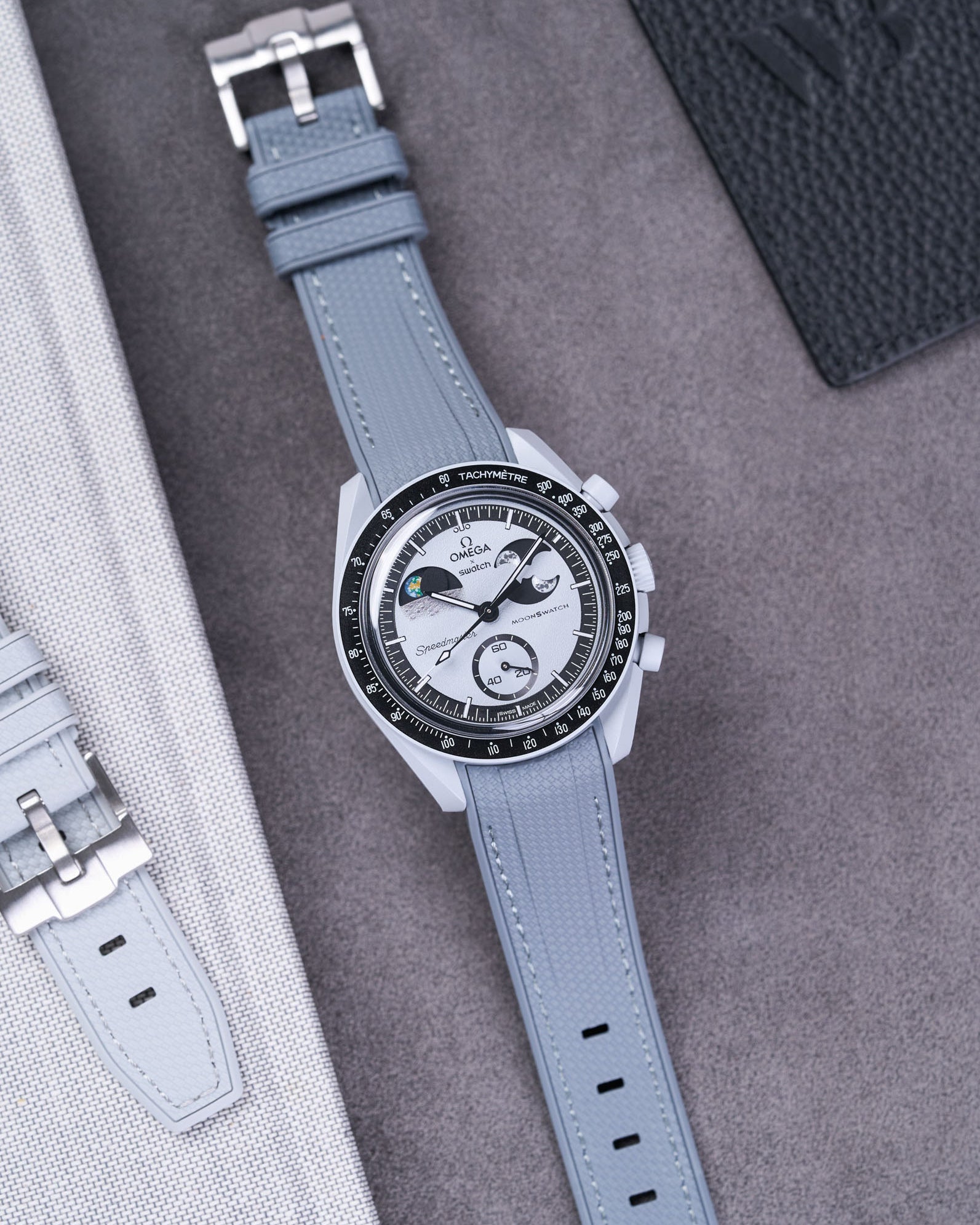 Flat lay of Vertech Omega X Swatch MoonSwatch Mission to EarthPhase with dark grey rubber strap, watch facing up with clasp visible