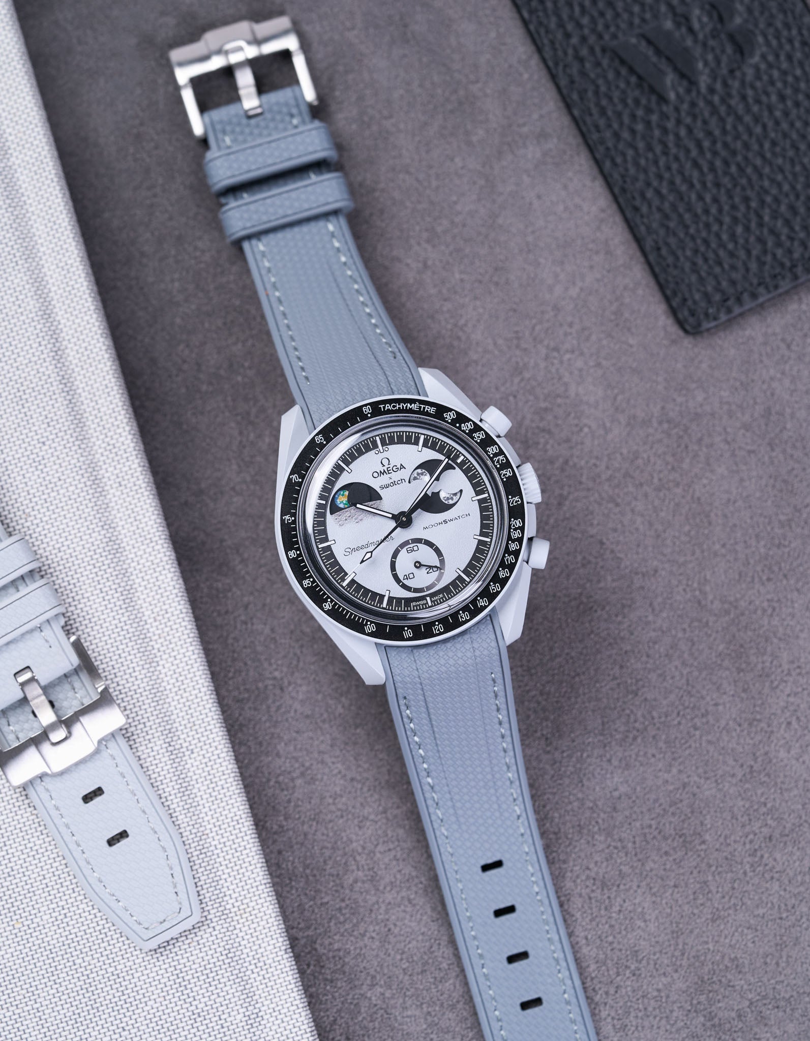 Flat lay of Vertech Omega X Swatch MoonSwatch Mission to EarthPhase with dark grey rubber strap, watch facing up with clasp visible