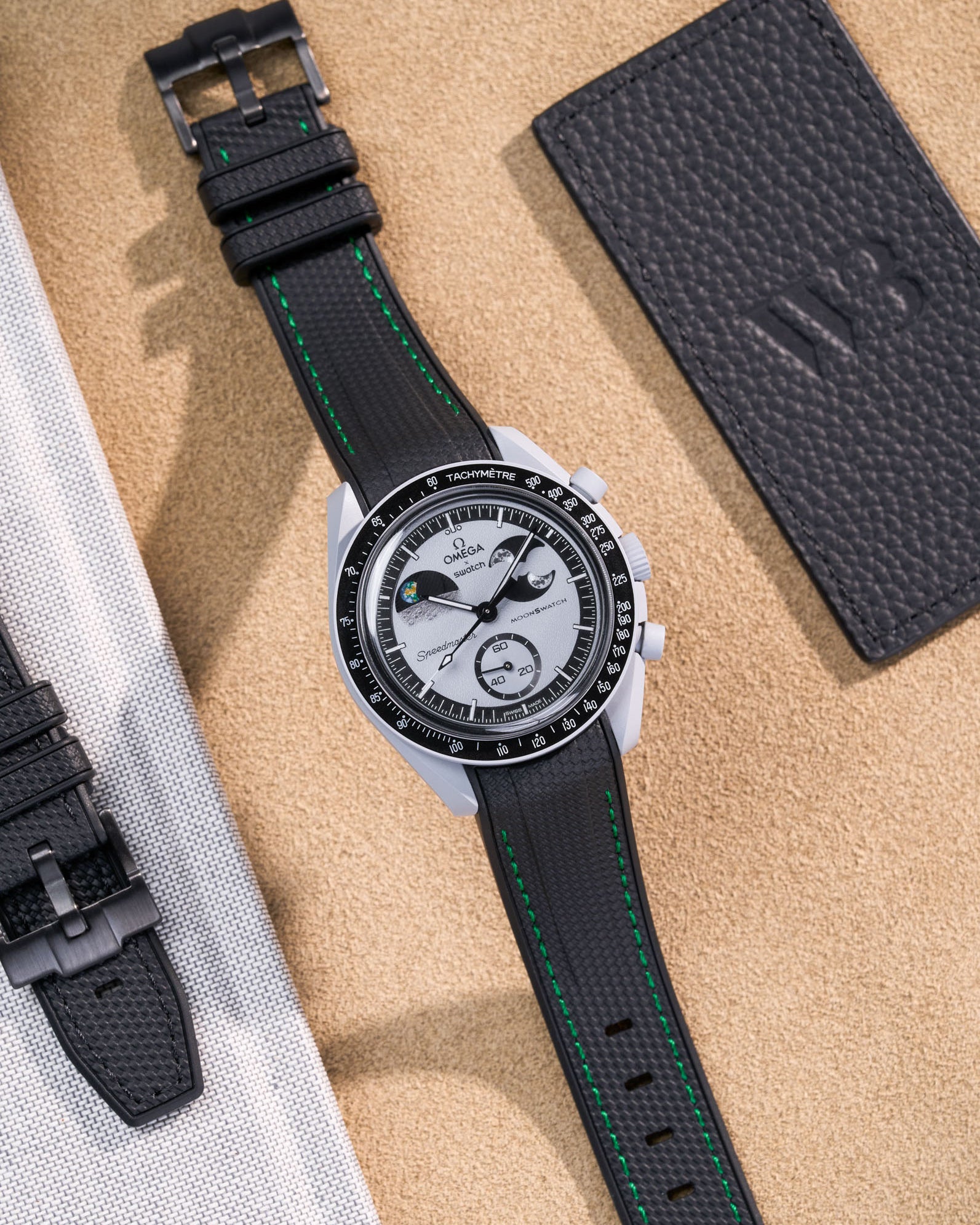 Flat lay of MoonSwatch Mission to EarthPhase with black rubber strap with green stitches, watch facing up with clasp visible