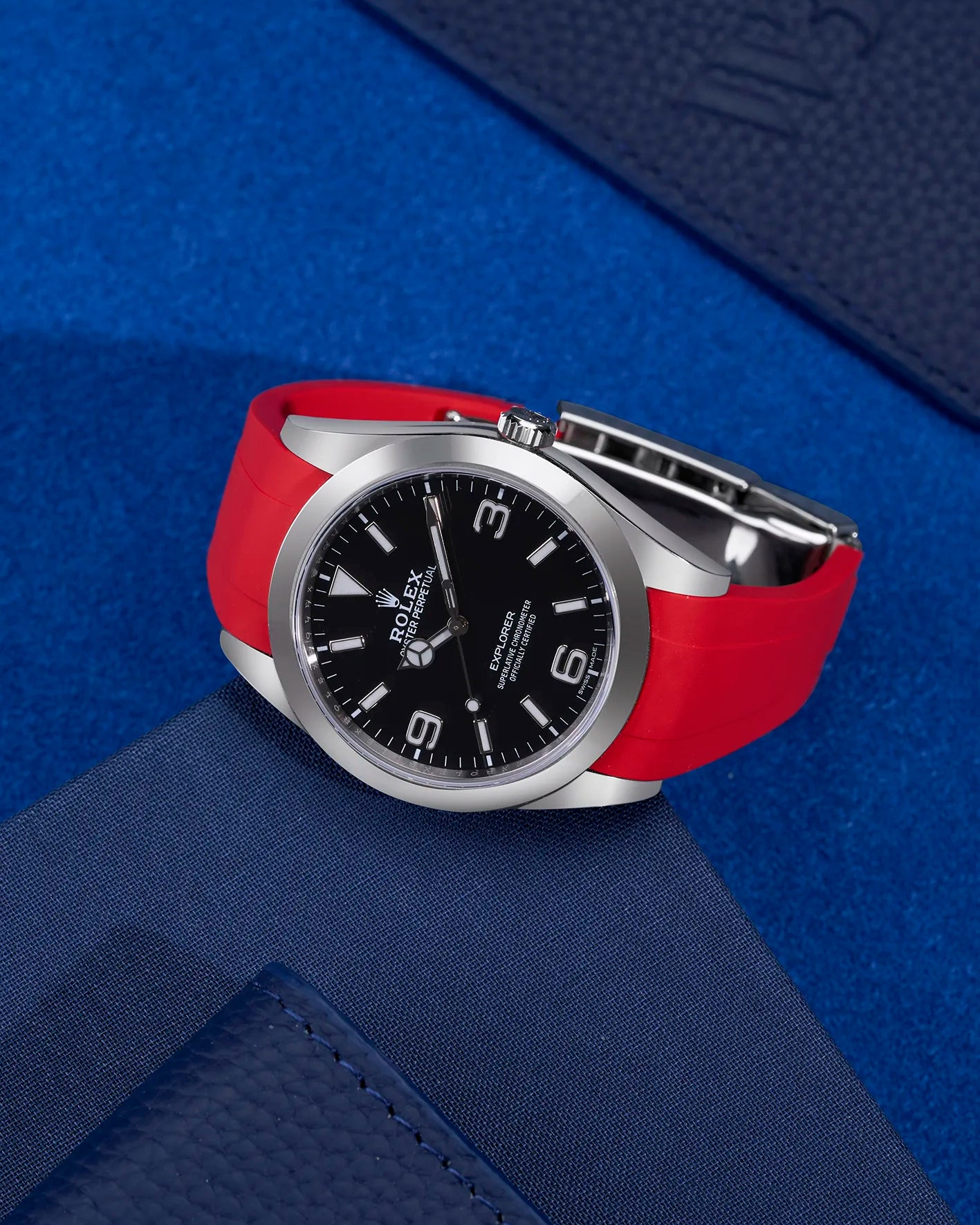 Rolex Explorer 214270 paired with red rubber strap and original clasp – flat lay on blue background