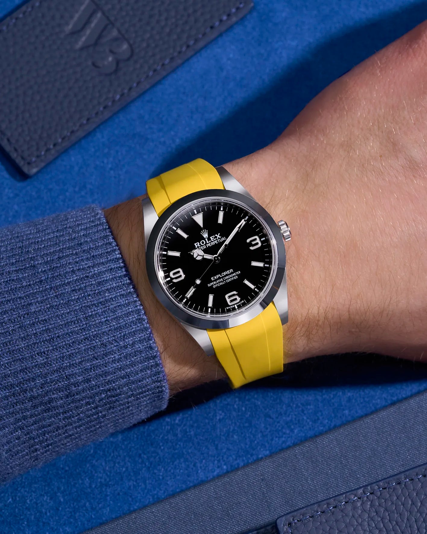 Rolex Explorer 214270 on wrist with integrated yellow rubber strap and original clasp – blue contrast backdrop