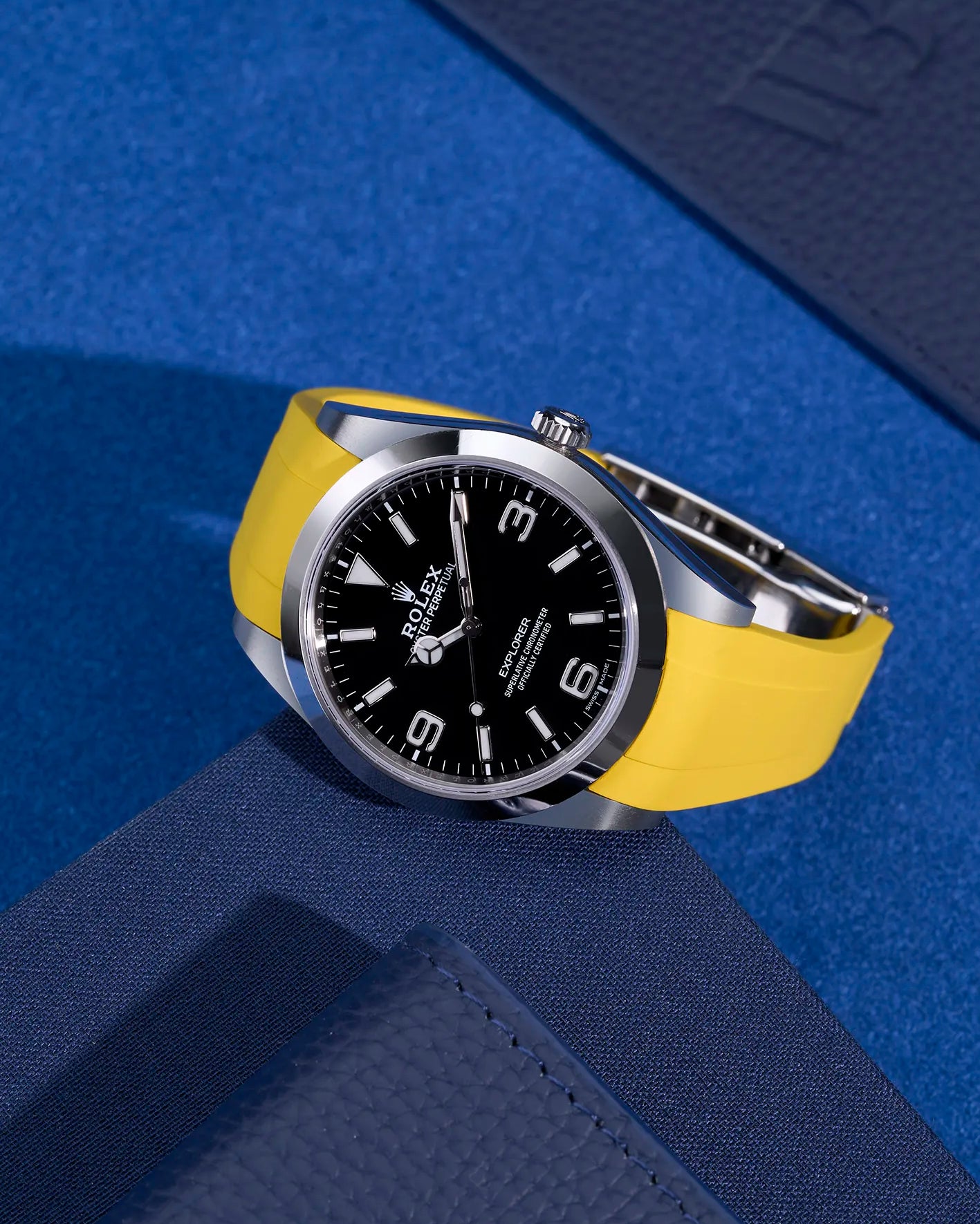 Yellow integrated rubber strap with original clasp mounted on Rolex Explorer 214270 – flat lay on navy blue surface