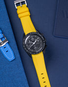 MoonSwatch Mission to Moonphase new Moon with vertech yellow rubber strap placed on blue fabric surface next to blue pouch