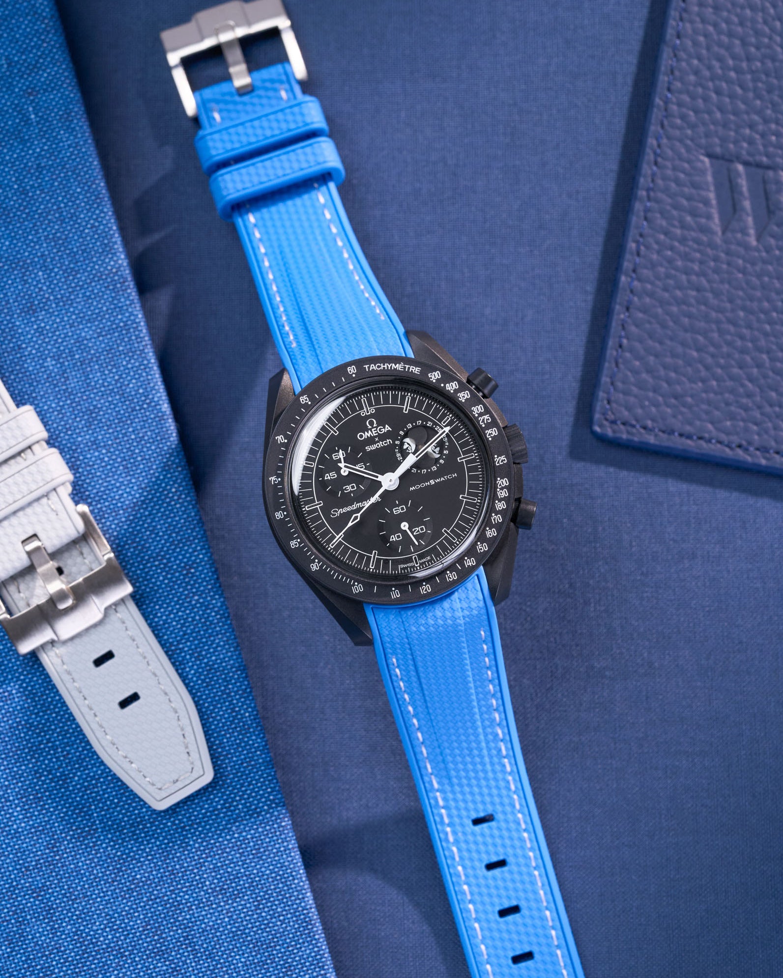 MoonSwatch Mission to Moonphase new Moon with vertech neptune blue rubber strap placed on blue fabric surface next to blue pouch