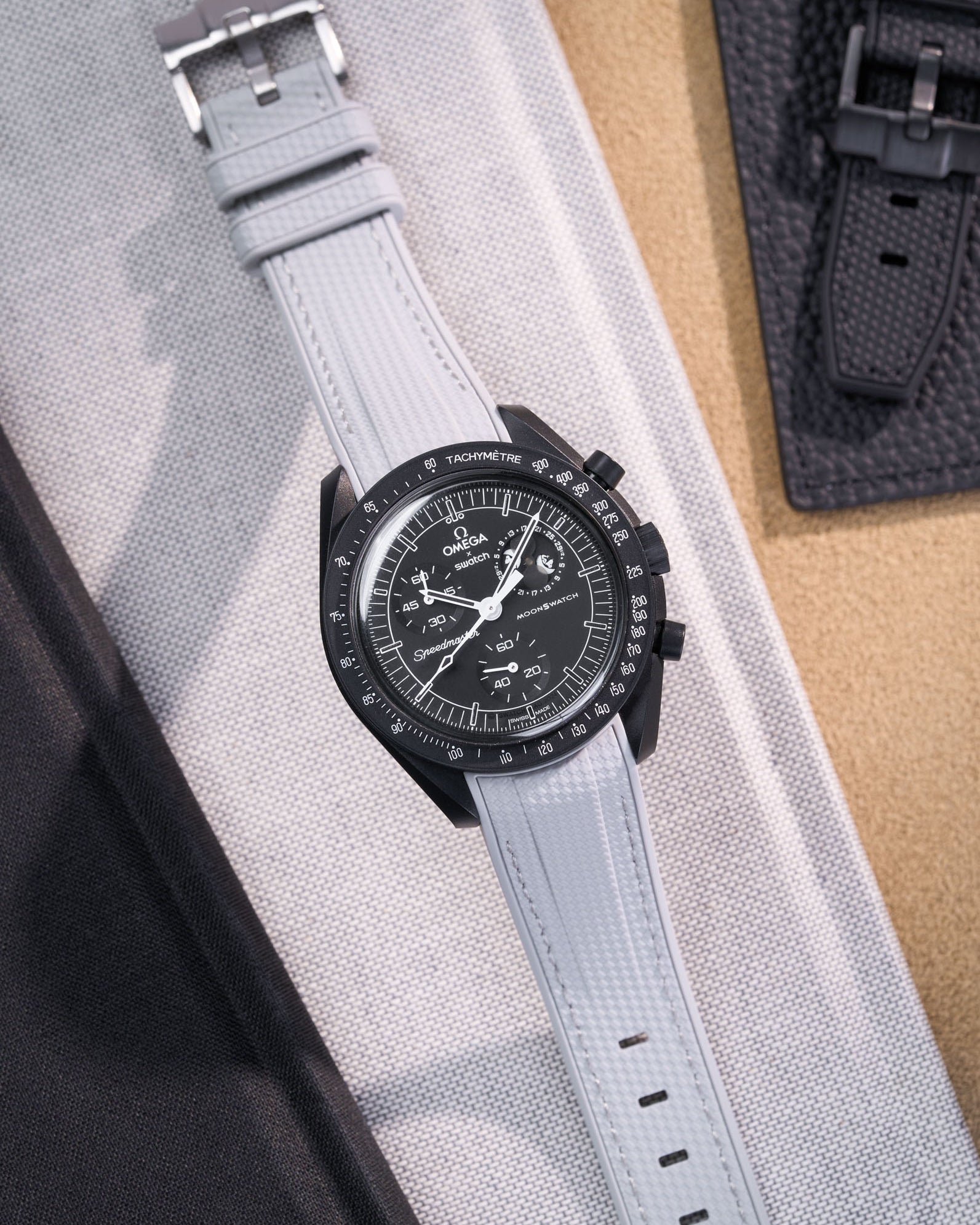 Black Omega X Swatch MoonSwatch Mission to The Moonphase - New Moon with a grey vertech rubber watch strap and a with detailed face on a grey background