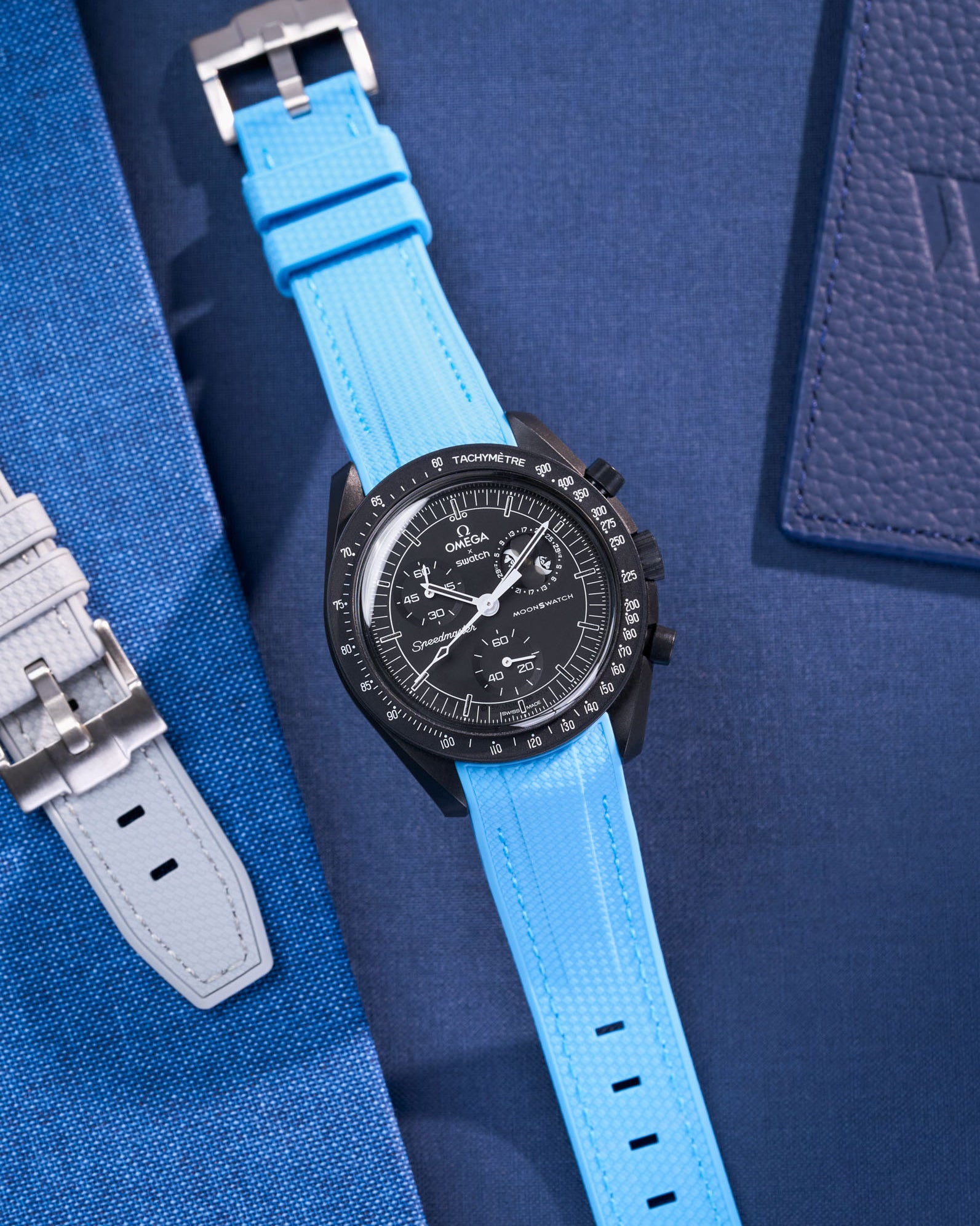 MoonSwatch Mission to Moonphase new Moon with Capri Blue rubber strap placed on fabric surface next to blue pouch