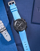 MoonSwatch Mission to Moonphase new Moon with Capri Blue rubber strap placed on fabric surface next to blue pouch