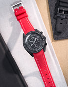 MoonSwatch Mission to Moonphase new Moon with vertech red rubber strap with white stitching placed on white fabric surface next to black pouch