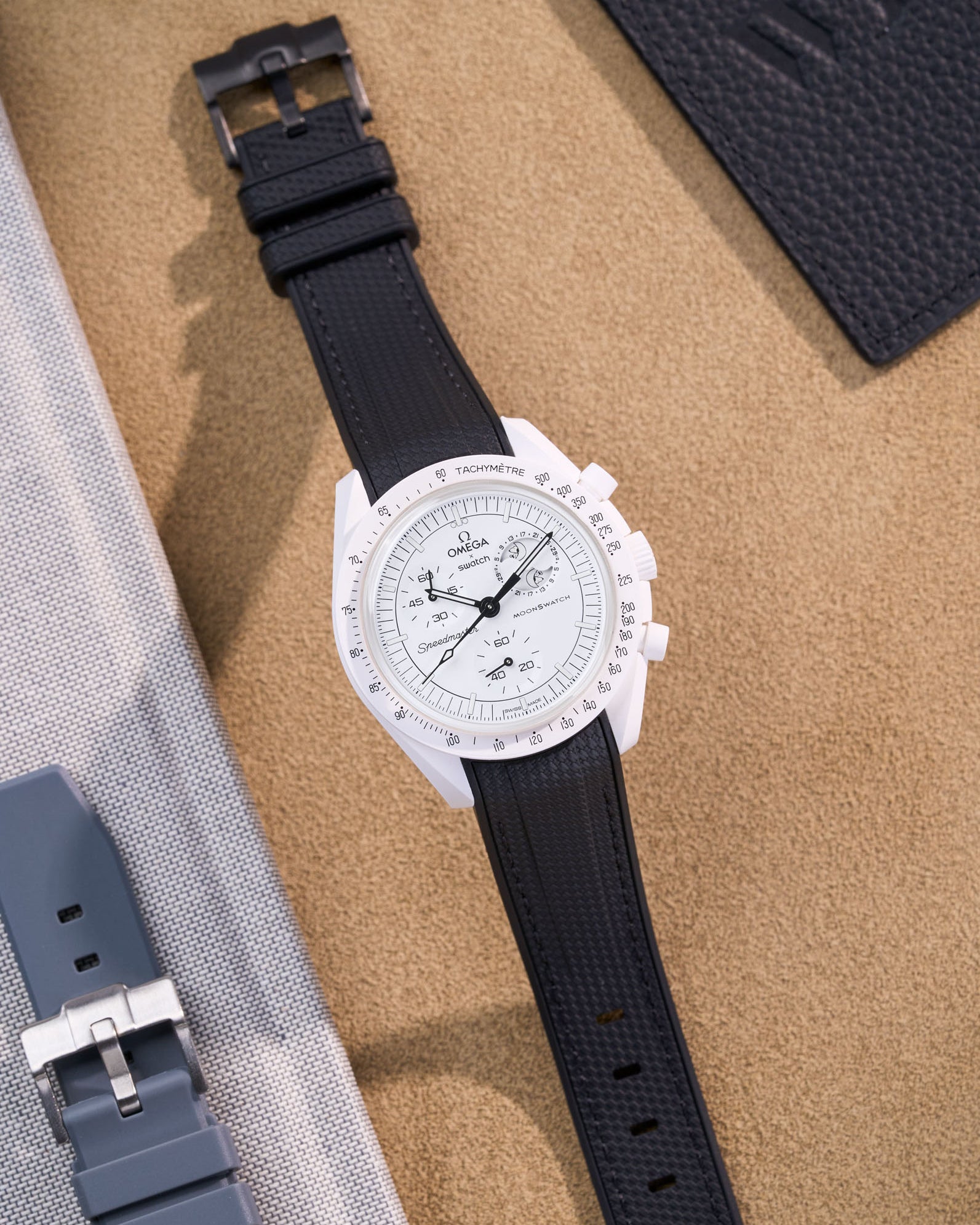 Omega Swatch MoonSwatch Mission to the Moonphase with black rubber strap flat lay on beige surface
