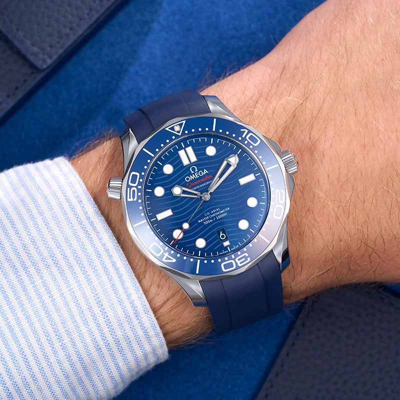 Wrist shot of Omega Seamaster 300 Diver with blue FKM rubber strap, shown in natural light with striped shirt and blue background