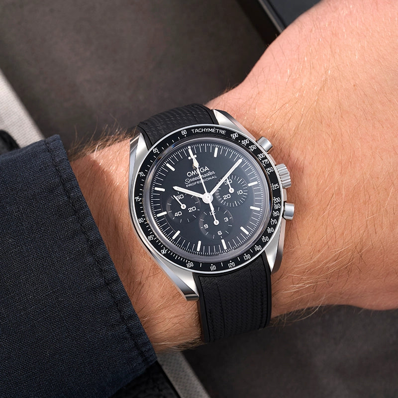 Wrist shot of Omega Speedmaster Professional with black FKM rubber strap, shown in natural light with dark shirt
