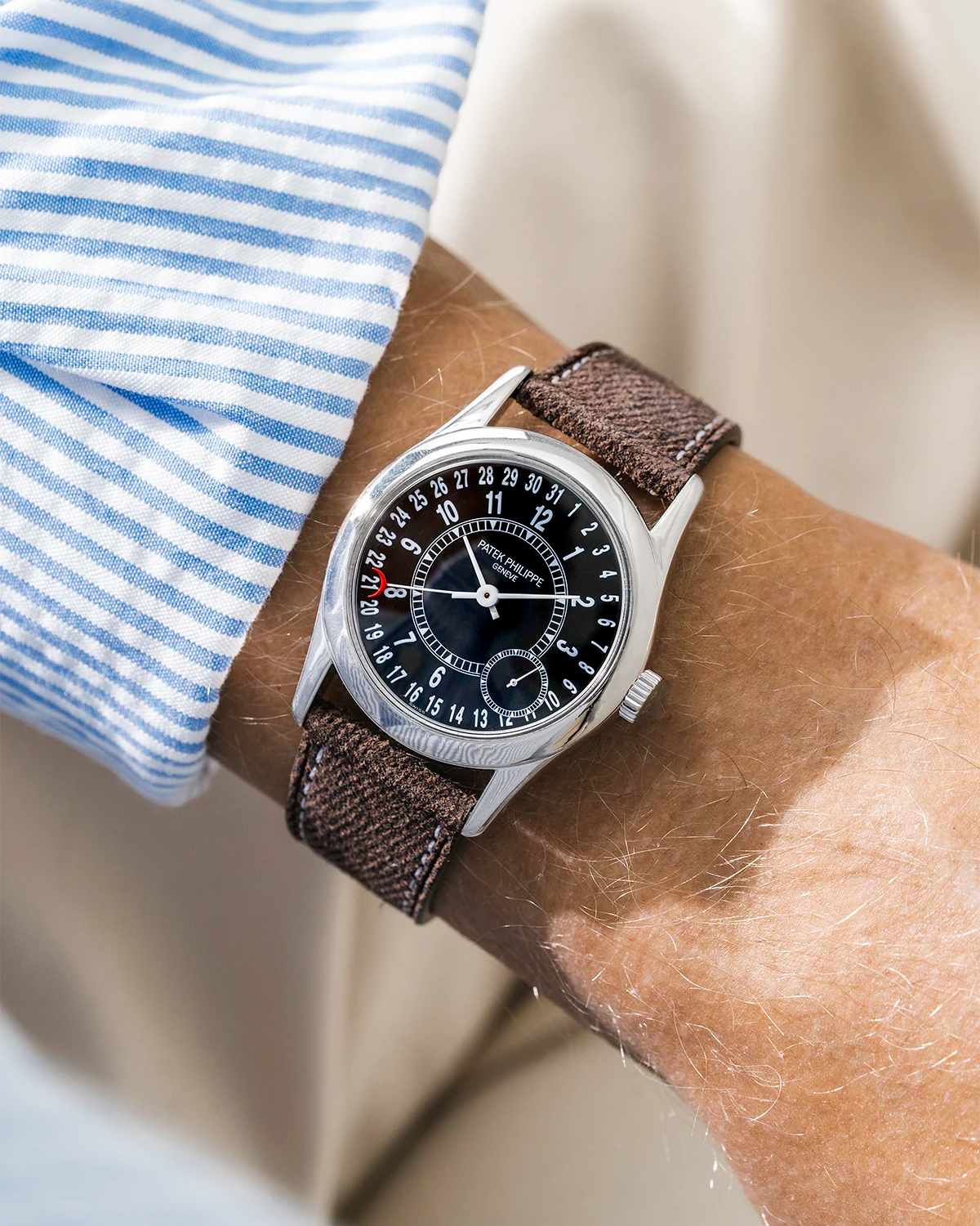 Patek Calatrava on a brown denim leather watch strap from Wristbuddys on a persons wrist wearing a blue striped shirt