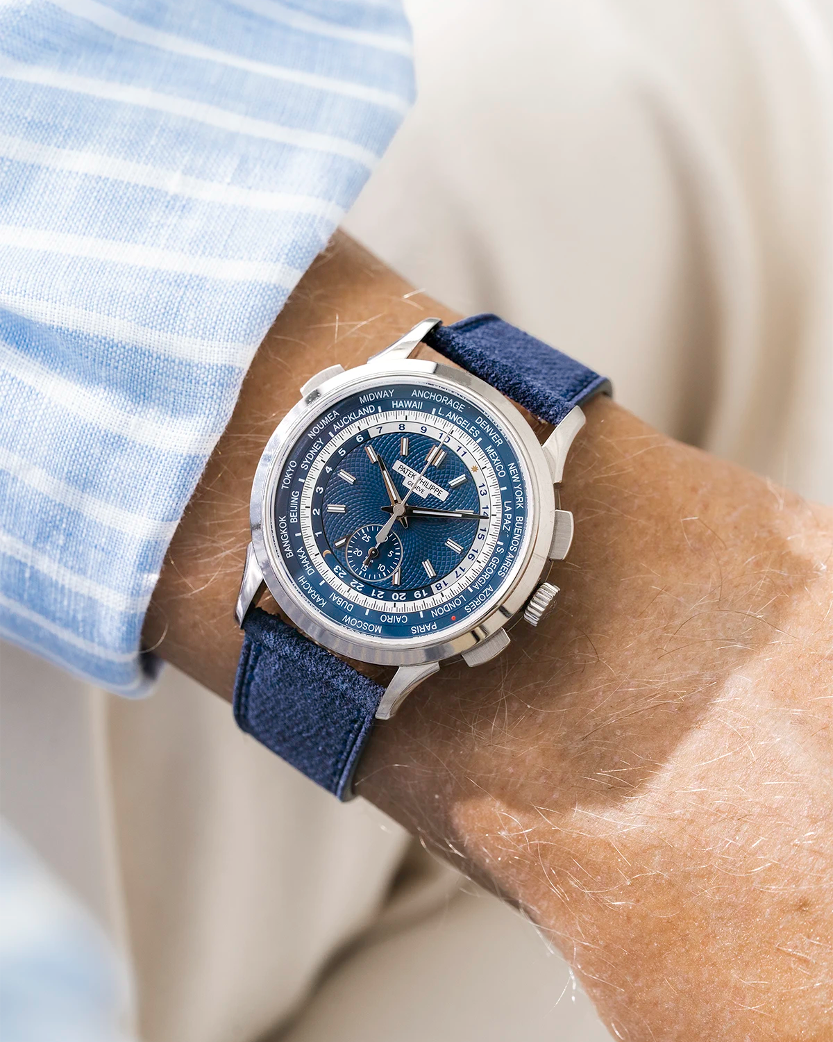 Patek Worldtimer on a navy blue denim leather watch strap from Wristbuddys on a persons wrist wearing a blue striped shirt