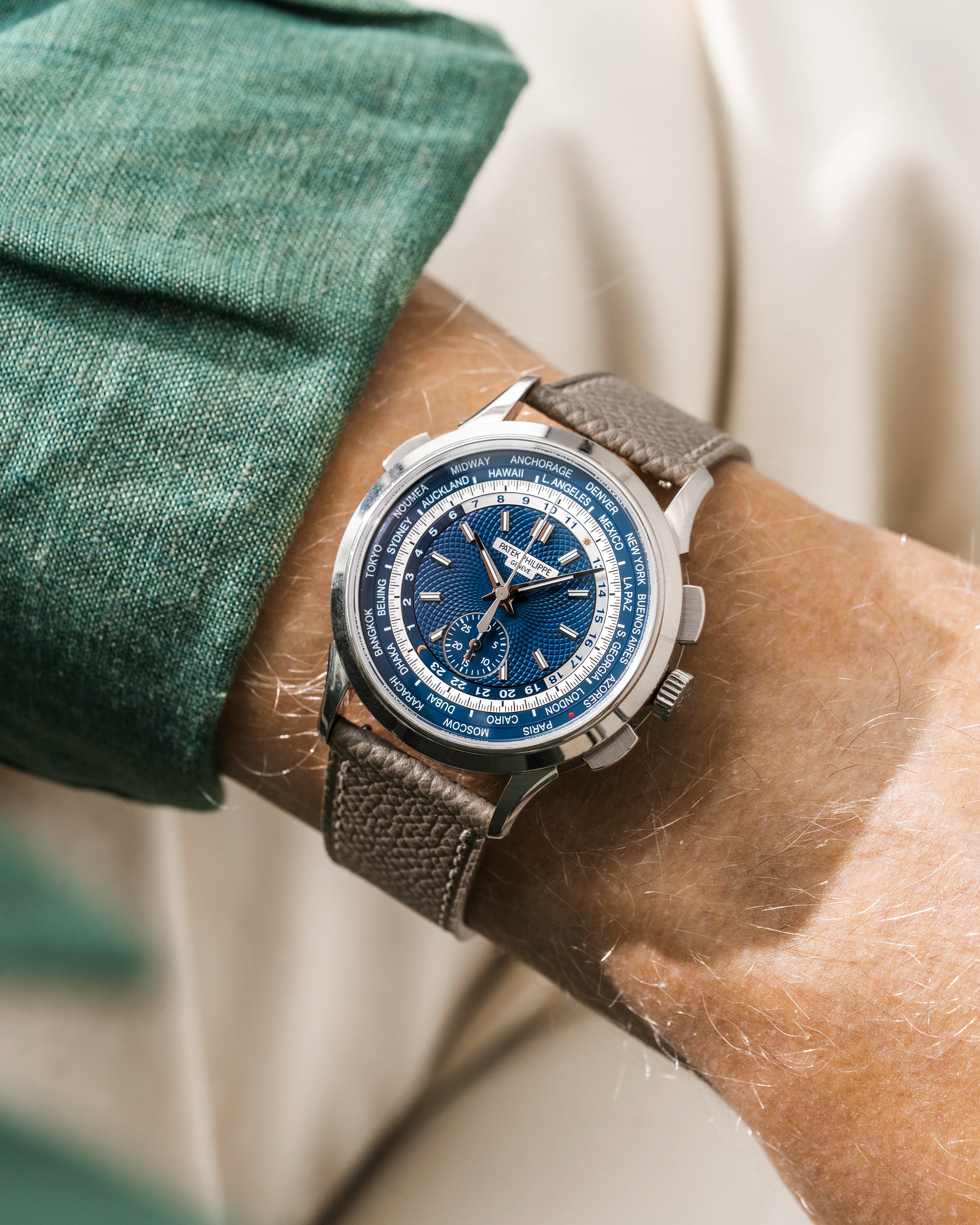 Patek Worldtimer with a blue face and grey epsom leather watch strap from Wristbuddys on a wrist, wearing a green shirt.