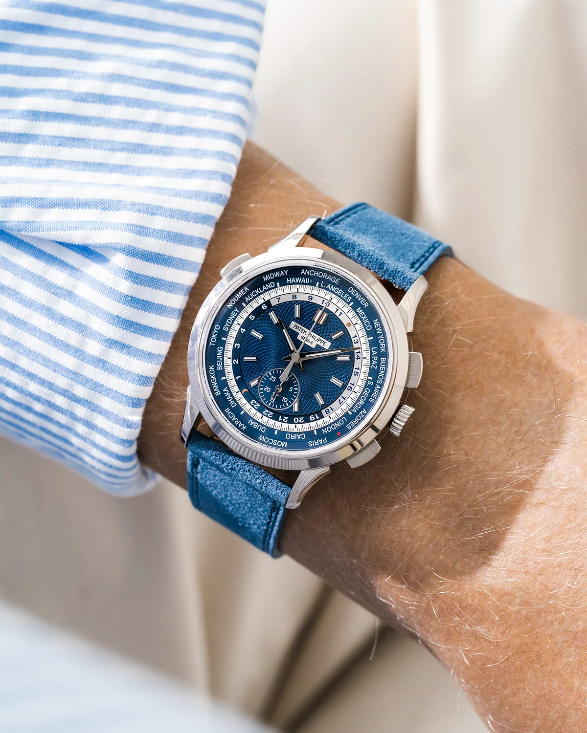 Blue Patek Worldtimer with a detailed face on a person's wrist, wearing a striped shirt and a baltic blue Suede watch stram from Wristbuddys