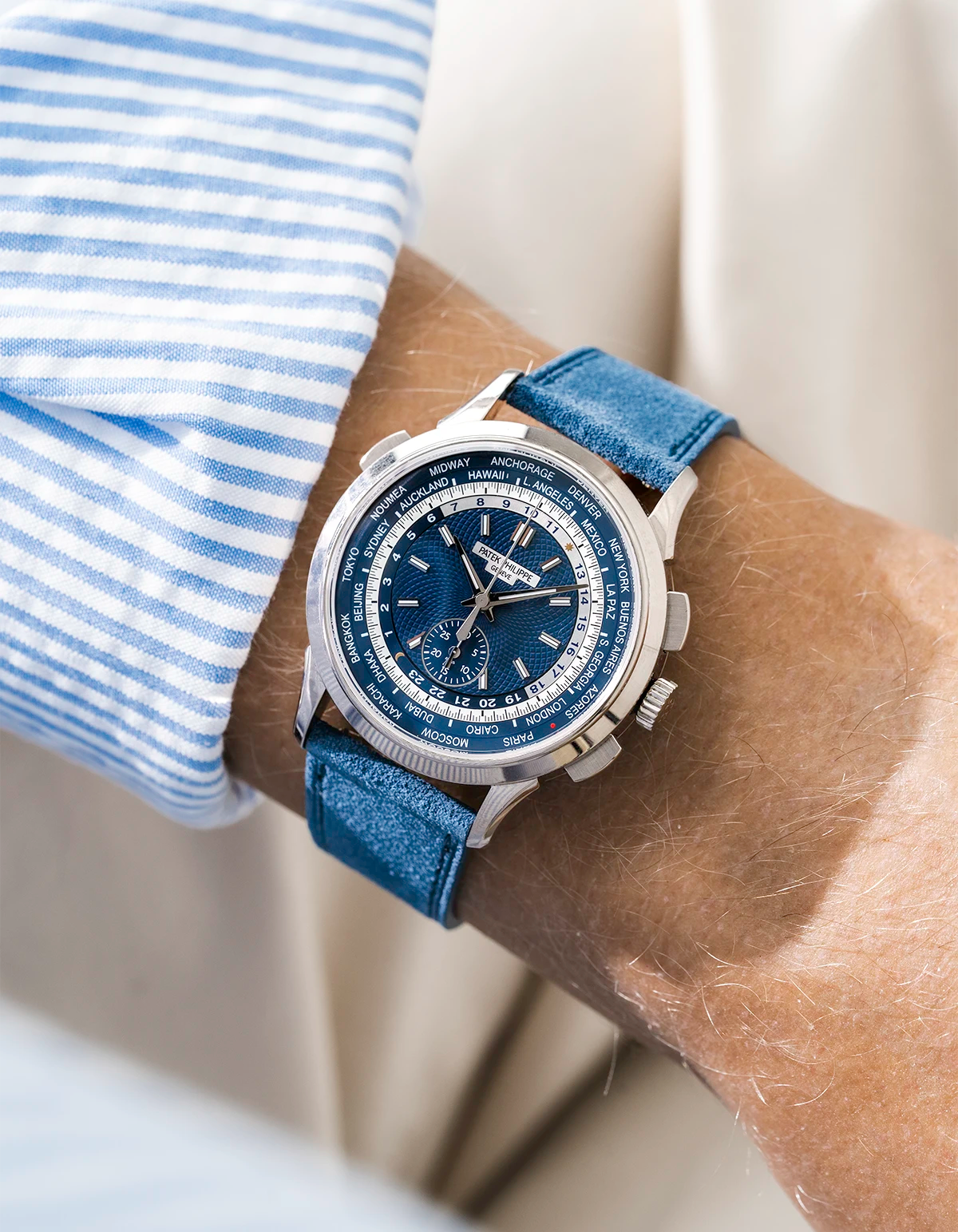 Blue Patek Worldtimer with a detailed face on a person's wrist, wearing a striped shirt and a baltic blue Suede watch stram from Wristbuddys