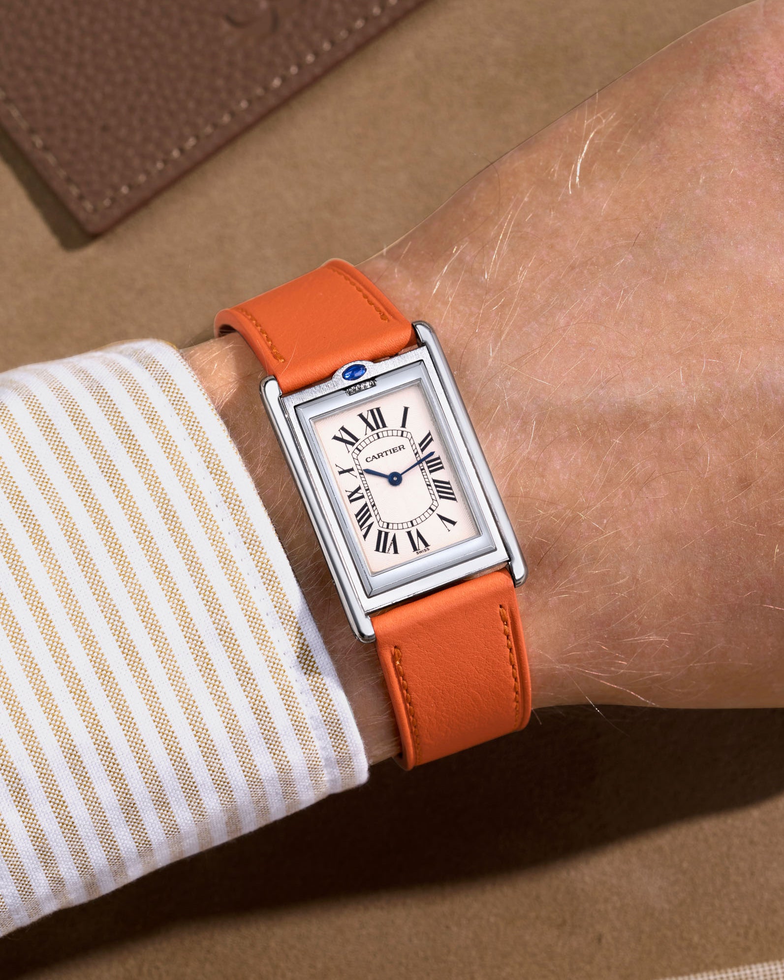 cartier basculante with white dial and with a orange cowhide leather watch strap on a beige background