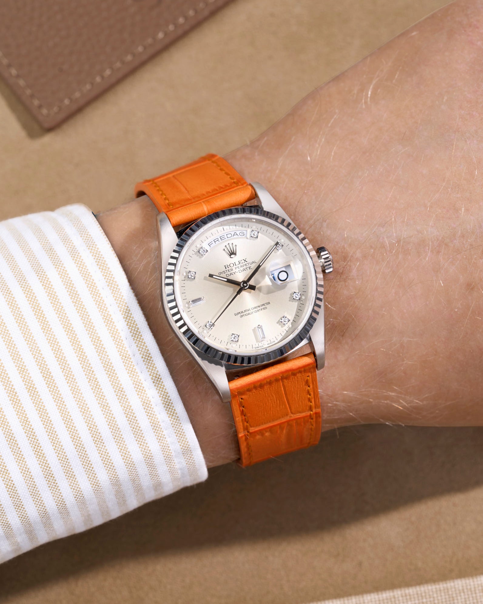 Rolex Daydate with diamond indexes watch with a orange alligator leather watch strap on a beige background