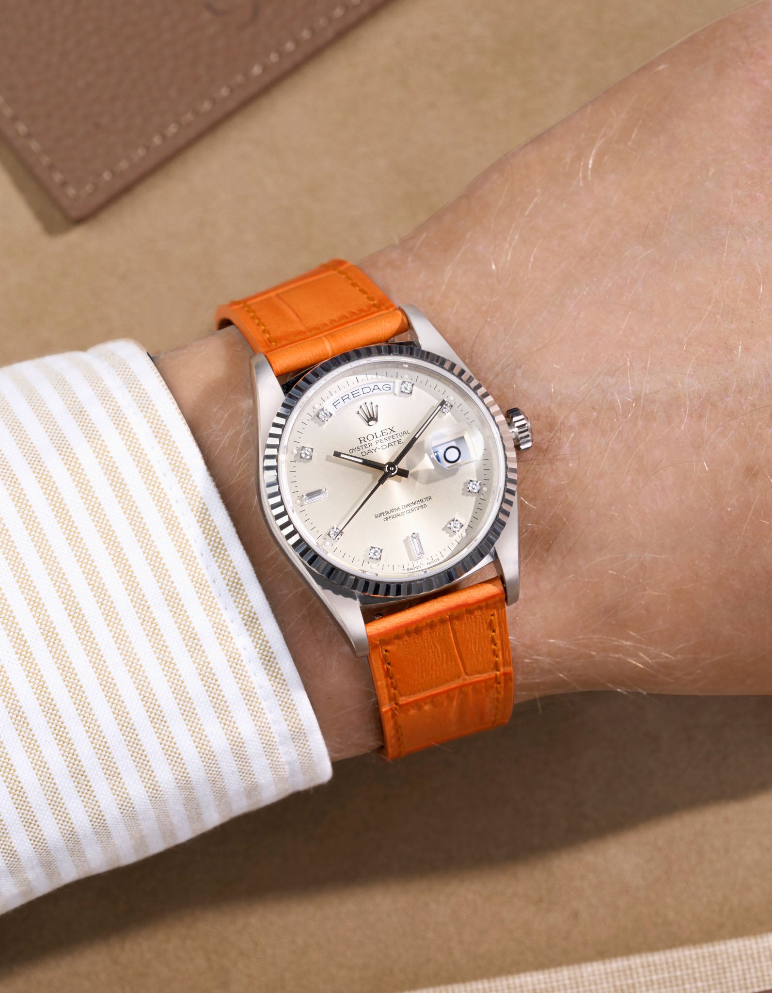 Rolex Daydate with diamond indexes watch with a orange alligator leather watch strap on a beige background