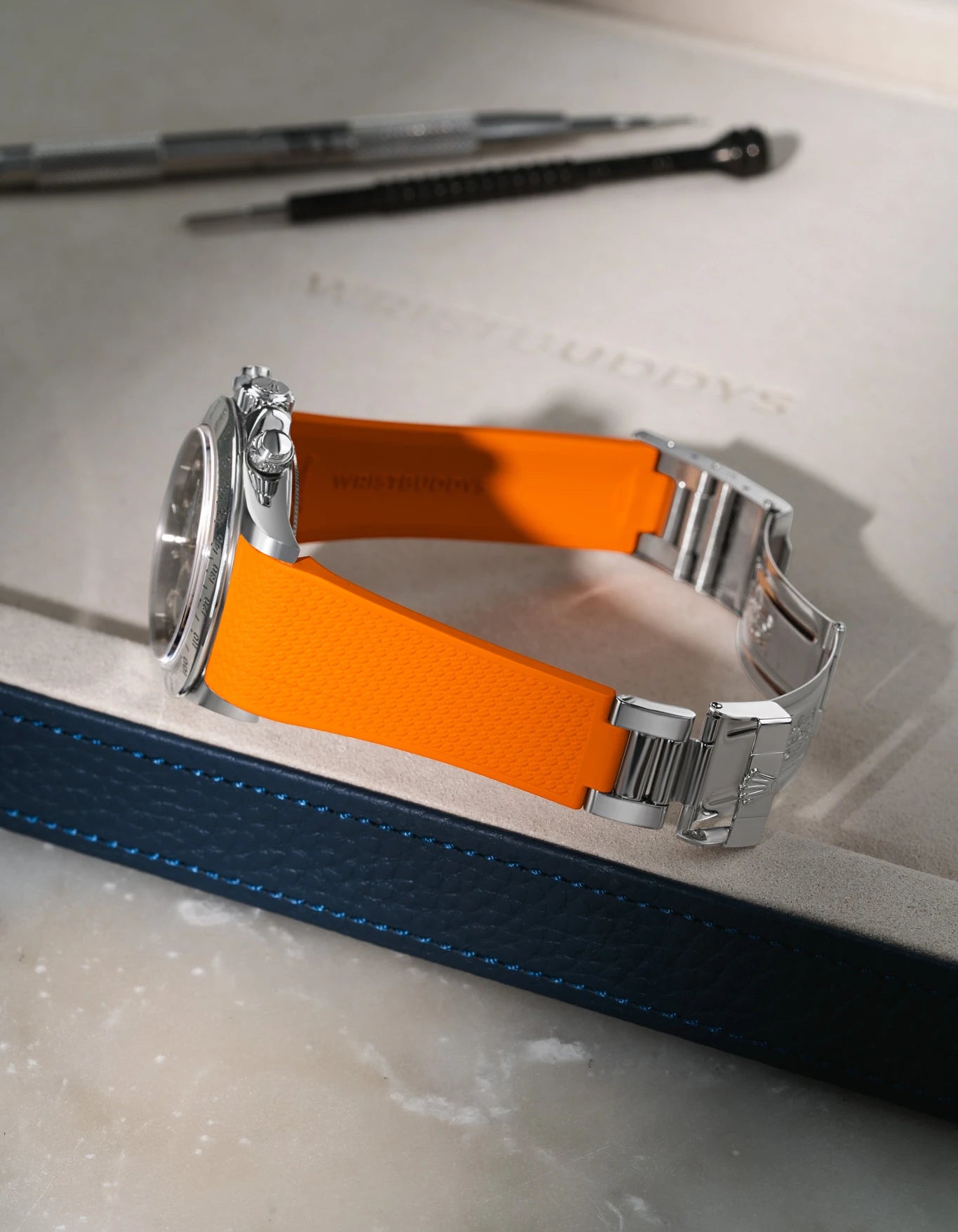 Bright Orange textured integrated FKM rubber strap for Rolex Daytona 16520, fits original clasp, resting on a leather valet tray.