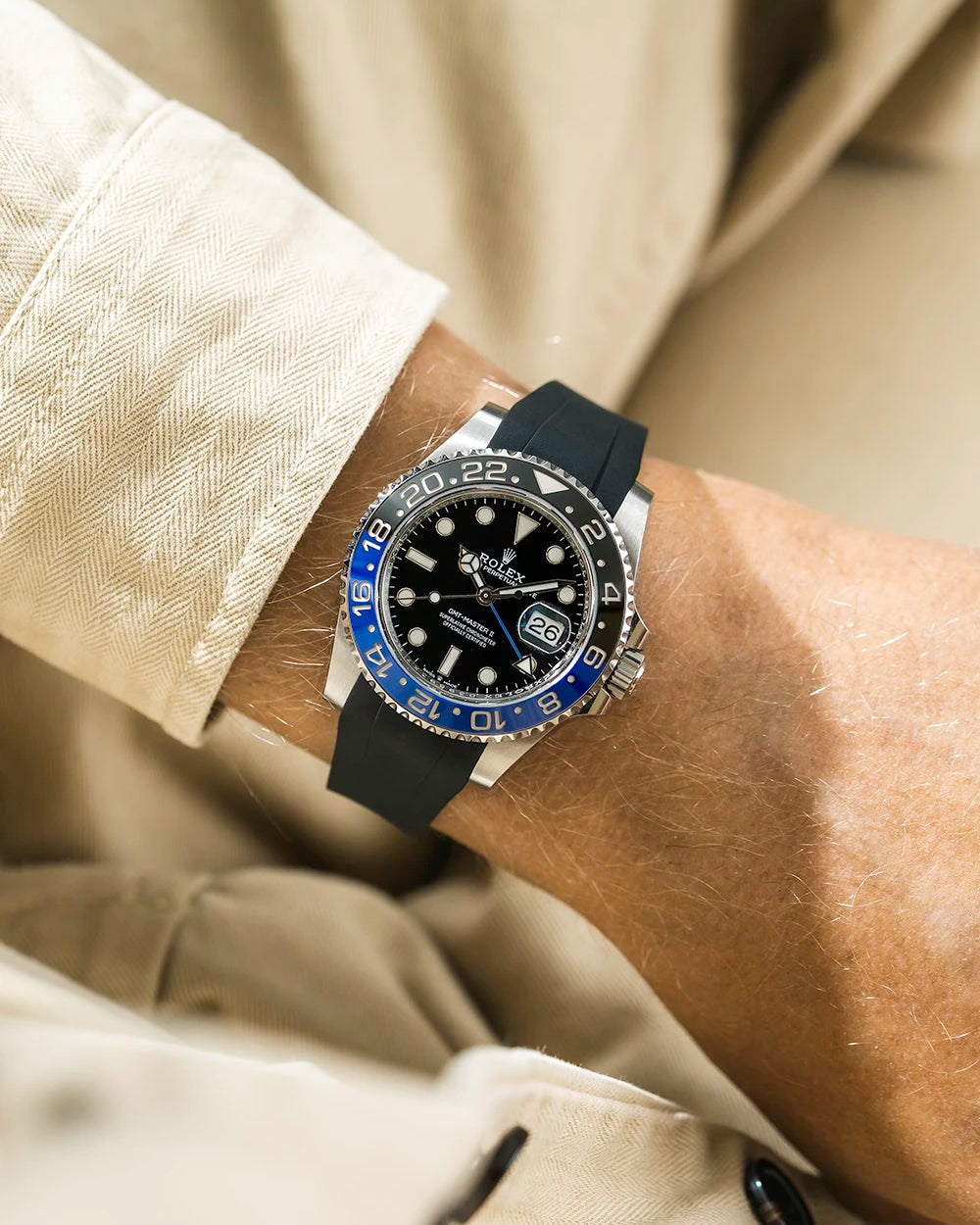 Close-up of a person wearing a Rolex GMT Master 2 Batman model watch with a beige jacket sleeve and a black FKM rubber watch strap from Wristbuddys