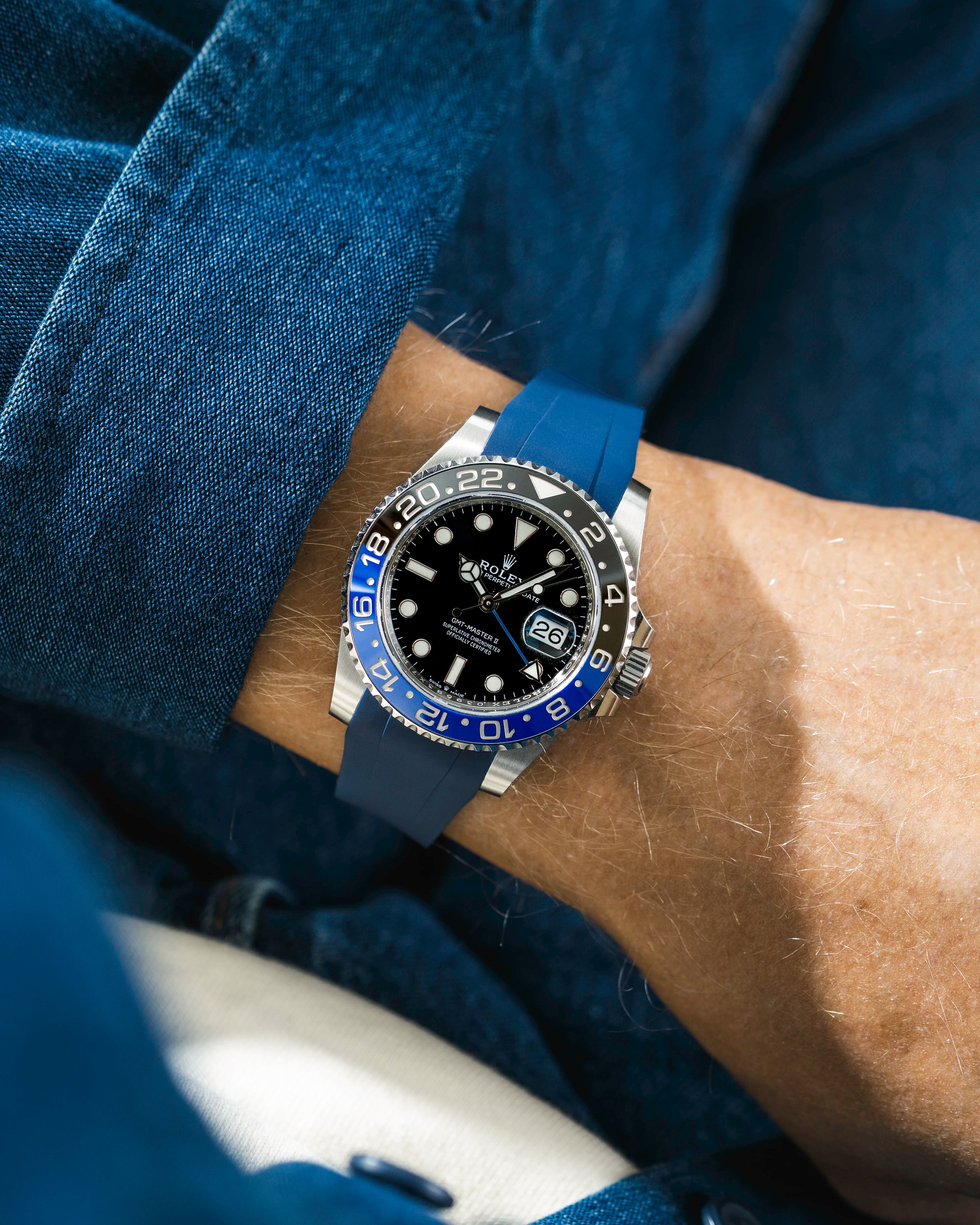 Close-up of a person wearing a Rolex GMT Master 2 Batman model watch with a blue jacket sleeve and a blue FKM rubber watch strap from Wristbuddys