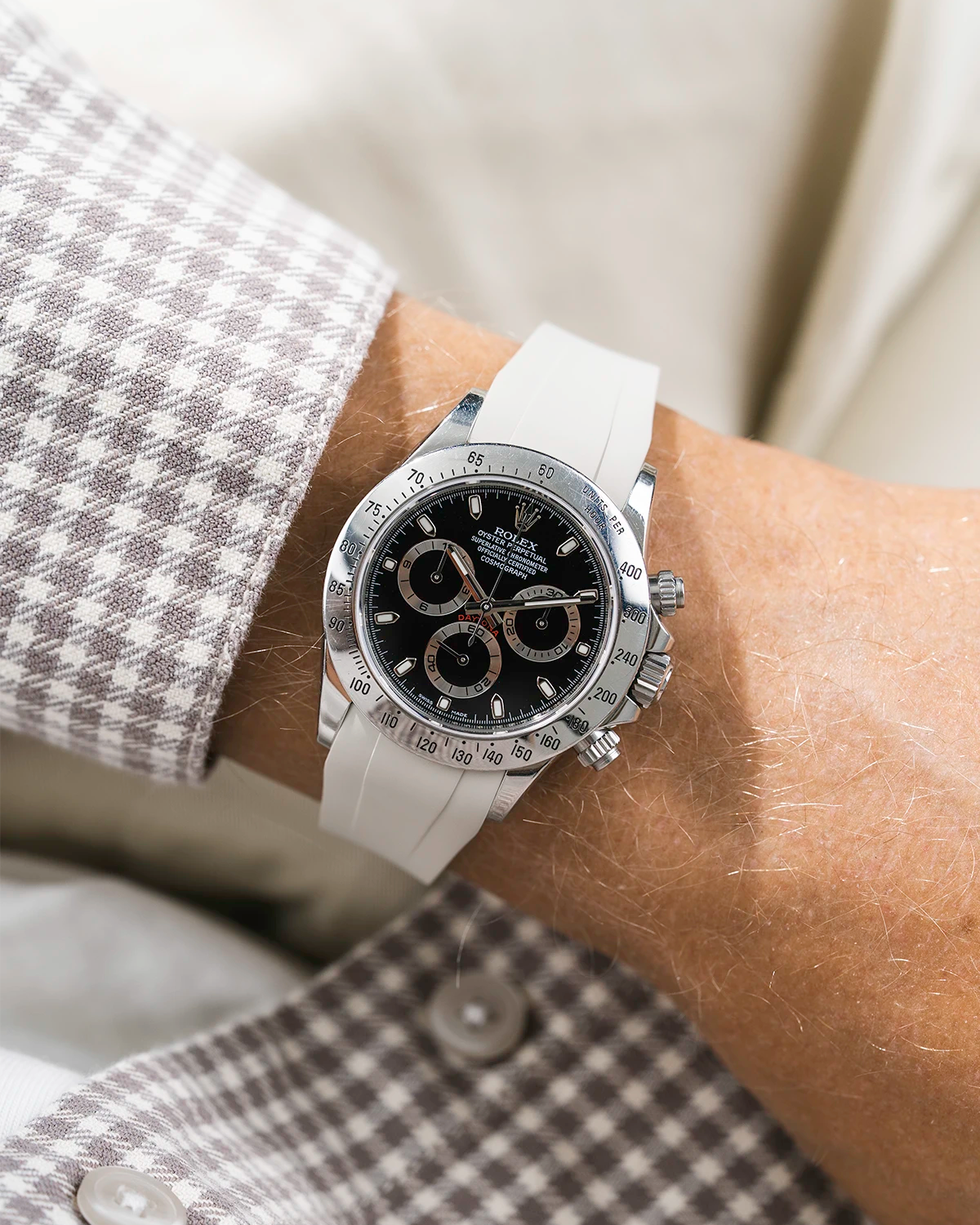 Close-up of a person wearing a black Rolex Daytona watch with a white jacket sleeve and a beige FKM rubber watch strap from Wristbuddys