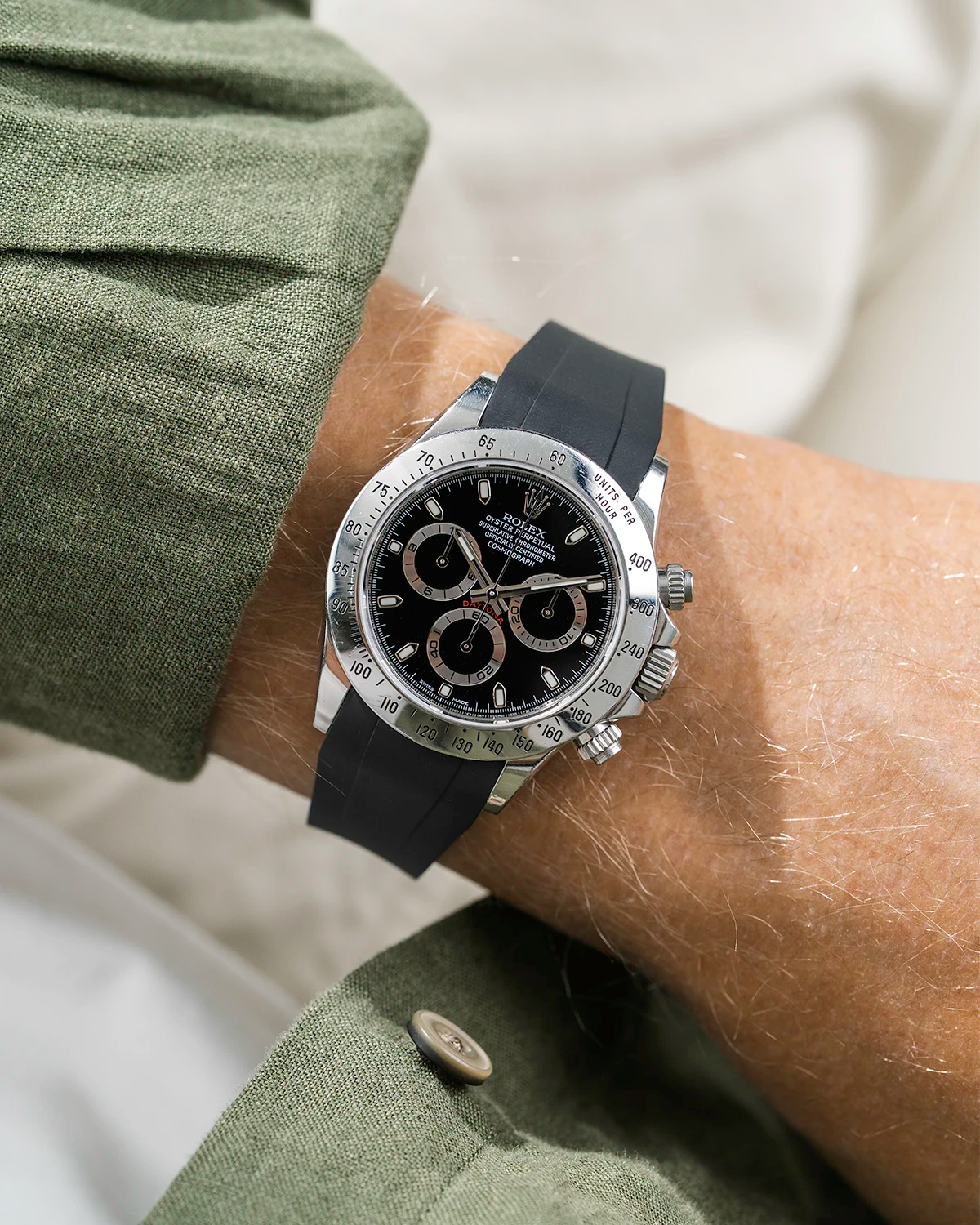 Close-up of a person wearing a black Rolex Daytona watch with a green jacket sleeve and a FKM rubber watch strap from Wristbuddys