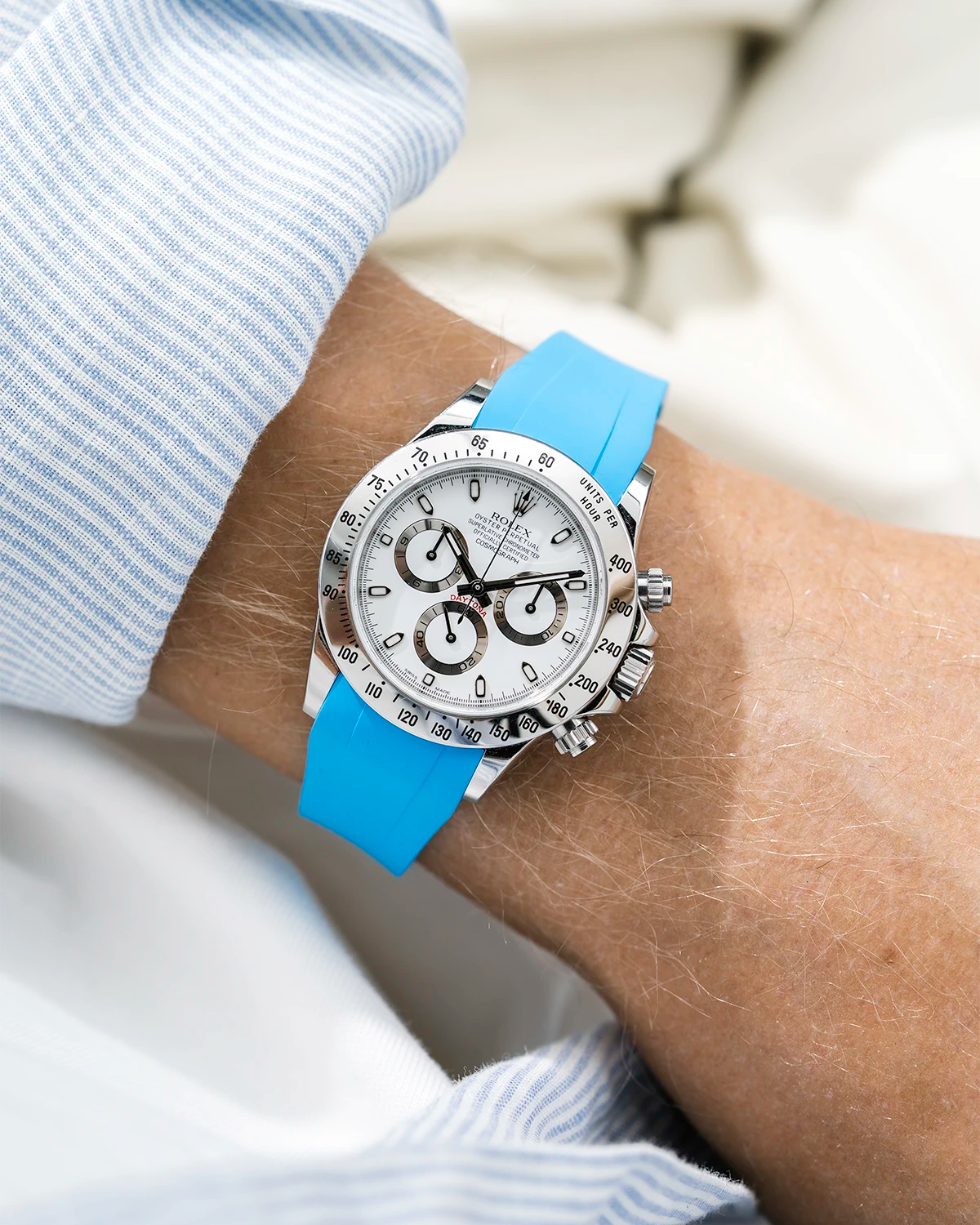 Close-up of a person wearing a white Rolex Daytona watch with a light blue stiped shirt sleeve and a tuquoise FKM rubber watch strap from Wristbuddys