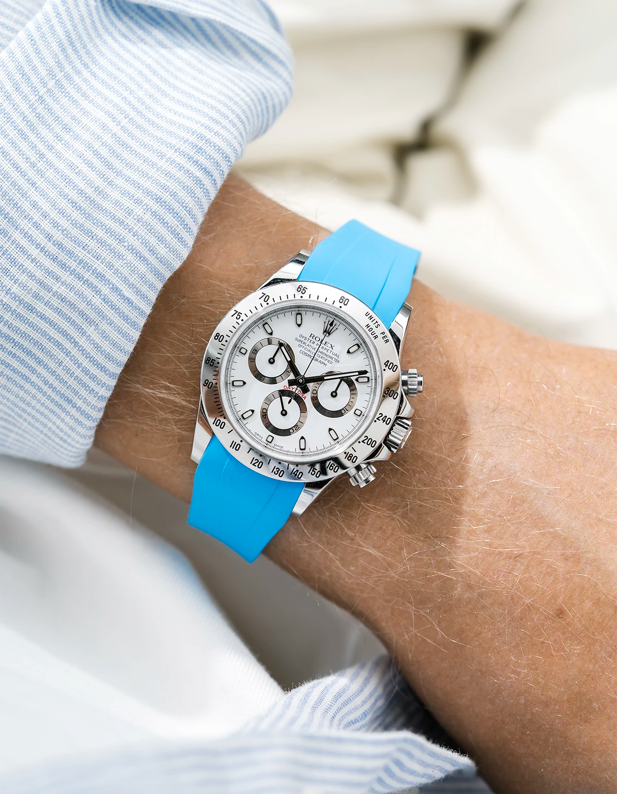 Close-up of a person wearing a white Rolex Daytona watch with a light blue stiped shirt sleeve and a tuquoise FKM rubber watch strap from Wristbuddys